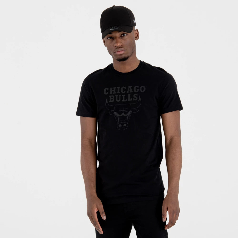 Chicago Bulls NBA Regular Black On Black T-Shirt, on-model view showing the black T-shirt with a subtle Bulls logo and CHICAGO BULLS text on the chest, paired with a black cap featuring a raised logo on the front.