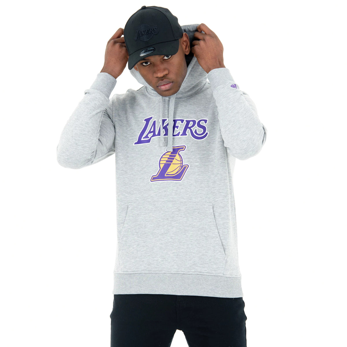 LA Lakers NBA Regular Grey Pullover Hoodie, on-model view showing the purple and yellow Lakers logo centred on the chest, a kangaroo pocket, long sleeves, and a grey drawstring hood being adjusted by the model.