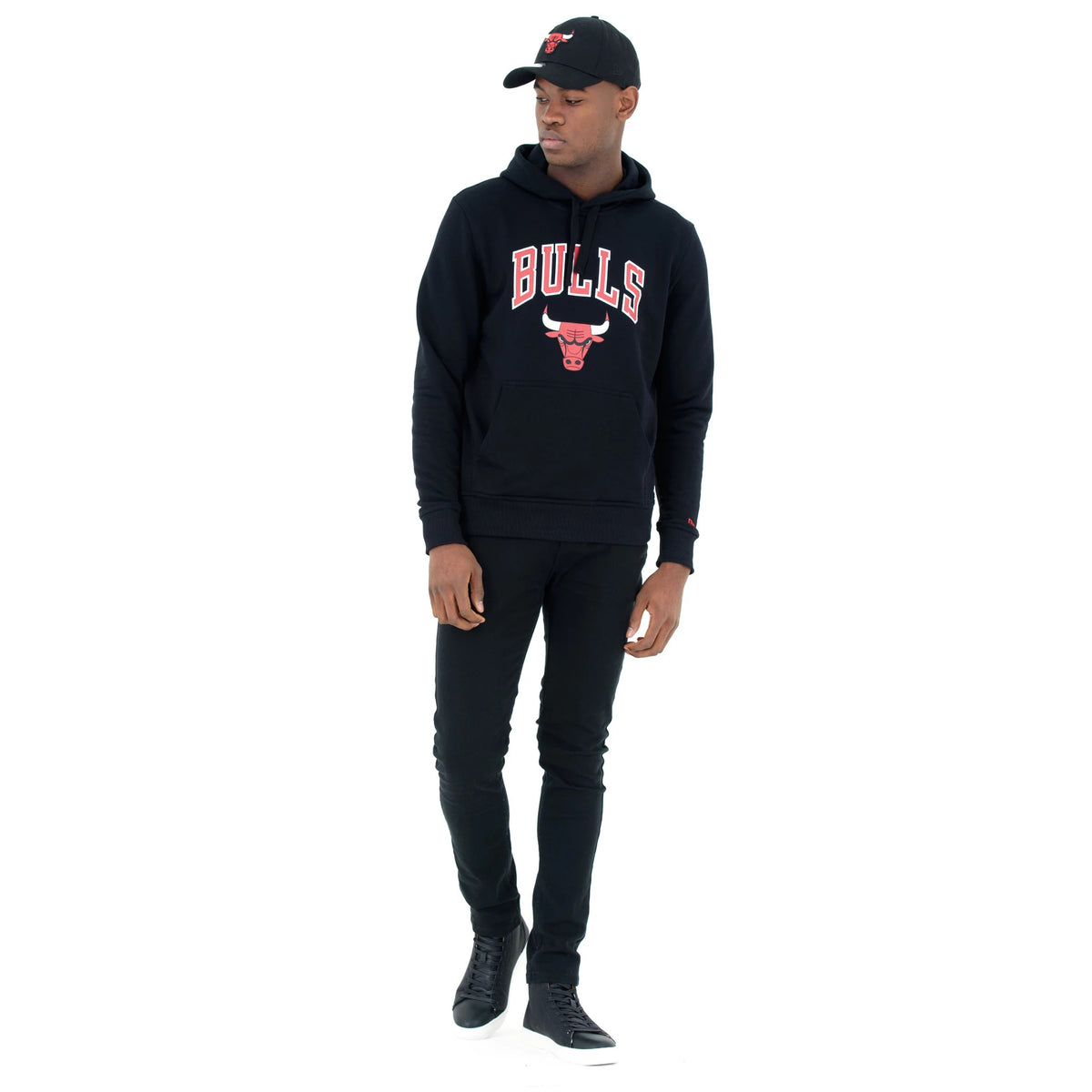Chicago Bulls NBA Regular Black Pullover Hoodie, on-model view showing the black hoodie with BULLS text and bull logo on the chest, paired with black trousers and black sneakers, a black cap with a raised Bulls logo on model's head.