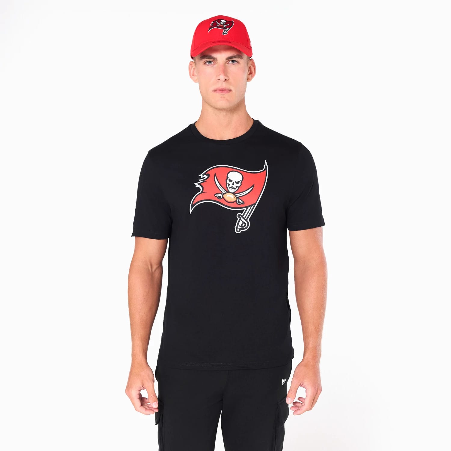 New Era Tampa Bay Buccaneers NFL Black T-Shirt, on-model view showing a black T-shirt with the red Buccaneers flag and skull logo printed prominently on the chest, worn with a red cap that has an embroidered logo on the front.