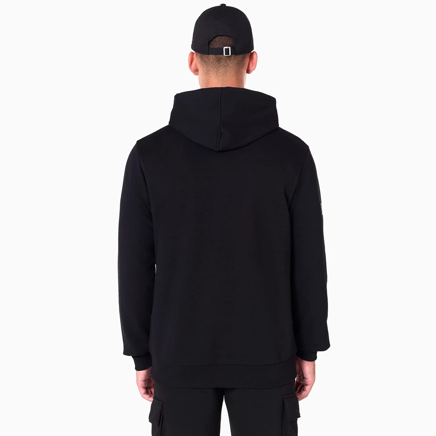NFL Shield Logo NFL Black Pullover Hoodie, rear view showing the plain black hoodie with a relaxed fit and the hood resting flat on the back, worn by a person with a black New Era cap featuring a debossed logo and eyelets.