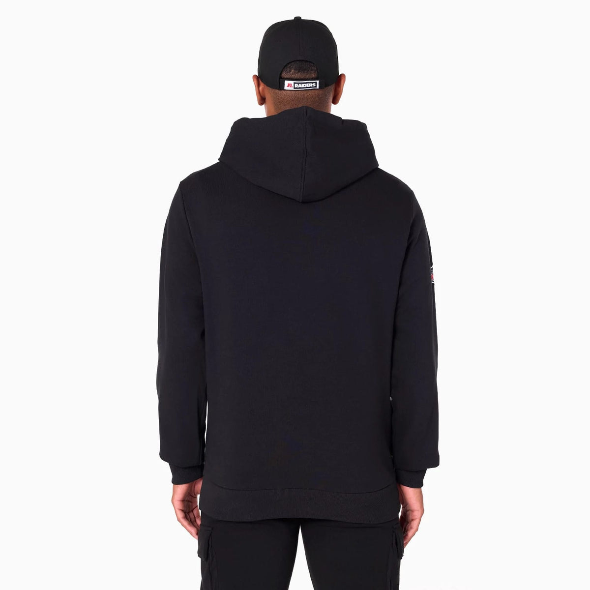 Las Vegas Raiders NFL Black Pullover Hoodie, rear view showing the plain black hoodie with its large hood draped over the shoulders, long sleeves, and a small logo patch on the upper left sleeve, worn by a person facing away.