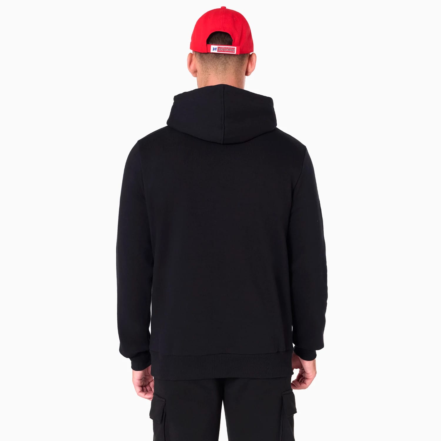 Tampa Bay Buccaneers NFL Black Pullover Hoodie, rear view showing the plain black back with an attached hood, worn by a model in black trousers and a bright red cap featuring a raised logo at the centre back.