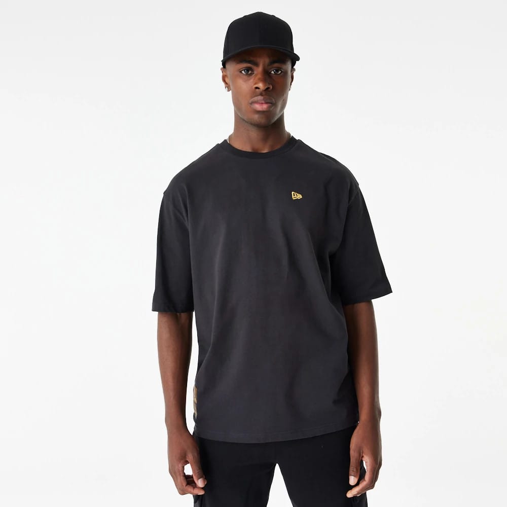 New Era Lifestyle 59FIFTY Black Oversized T-Shirt, on-model view showing the loose black T-shirt with a small raised gold New Era logo on the left chest, the sleeves reaching mid-arm length and the model wearing a black cap.