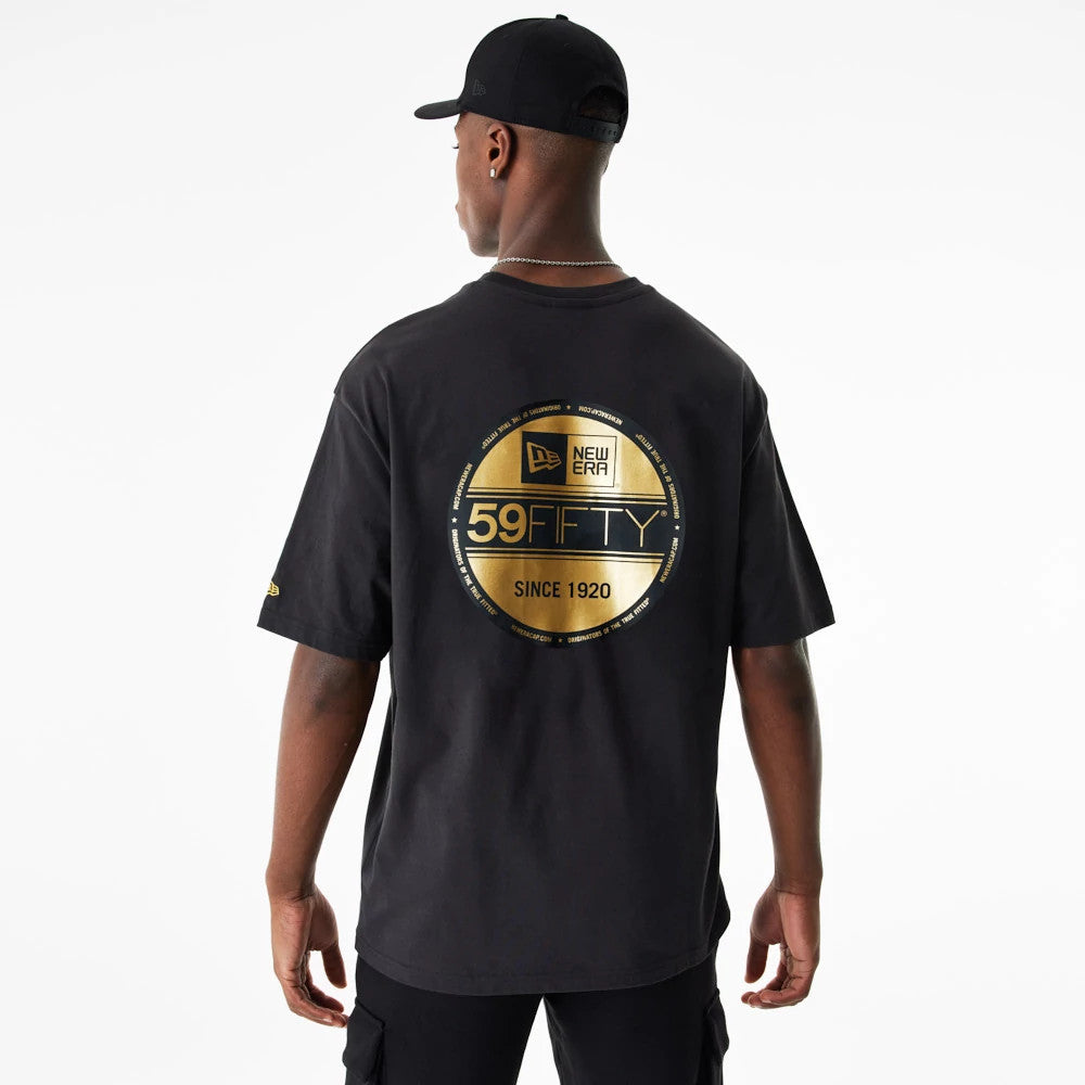 New Era Lifestyle 59FIFTY Black Oversized T-Shirt, rear view showing a large gold circular graphic centred on the back, with the debossed New Era logo above '59FIFTY' text, worn by a model also in a black cap.