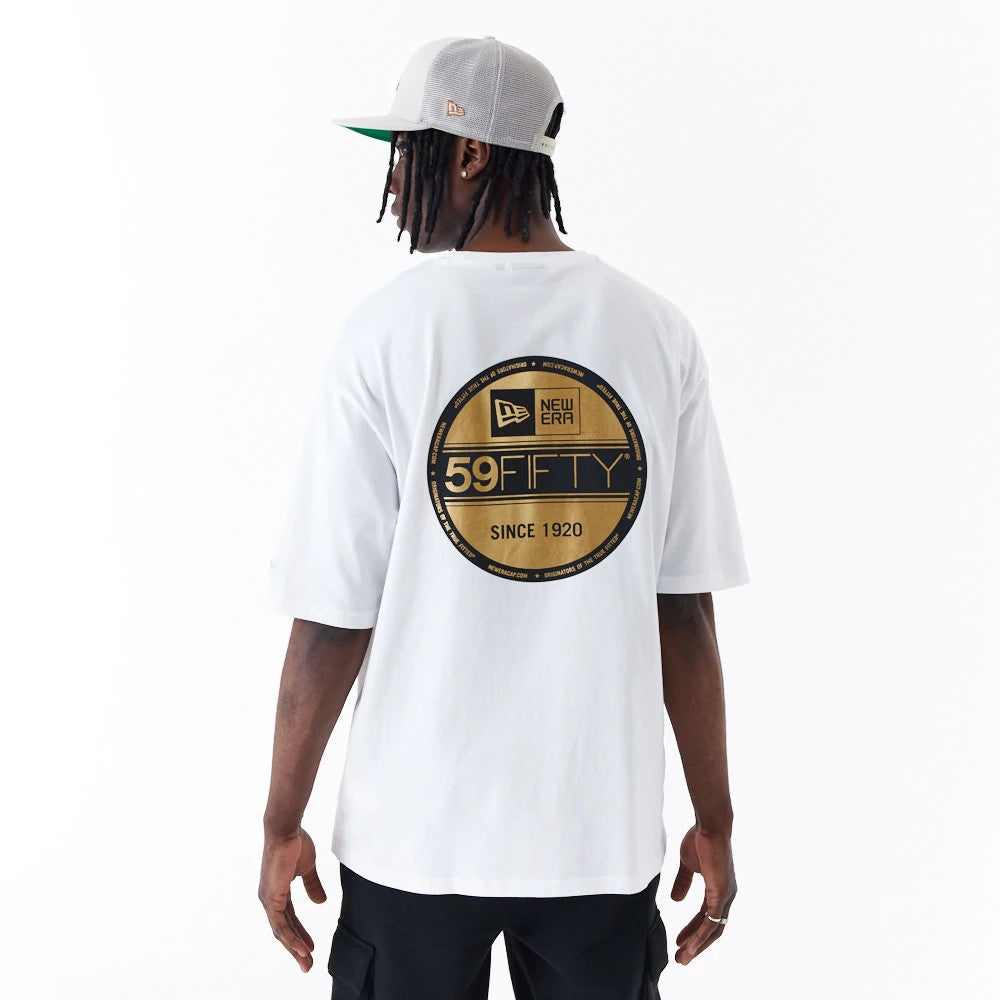 New Era Sticker White Oversized T-Shirt, rear view showing a large black and gold 59FIFTY logo centred on the back, worn by a person in black trousers and a grey cap with a raised New Era logo on the side.