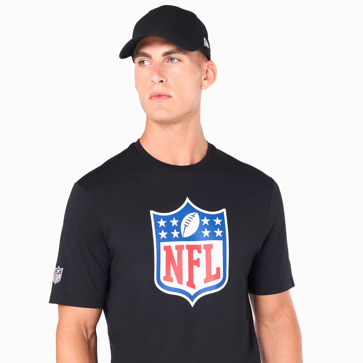 New Era NFL Shield Logo NFL Black T-Shirt, on-model view showing the large printed NFL shield logo centred on the chest, a smaller NFL logo on the left sleeve, and a plain black cap worn on the head with a raised New Era logo on the side.