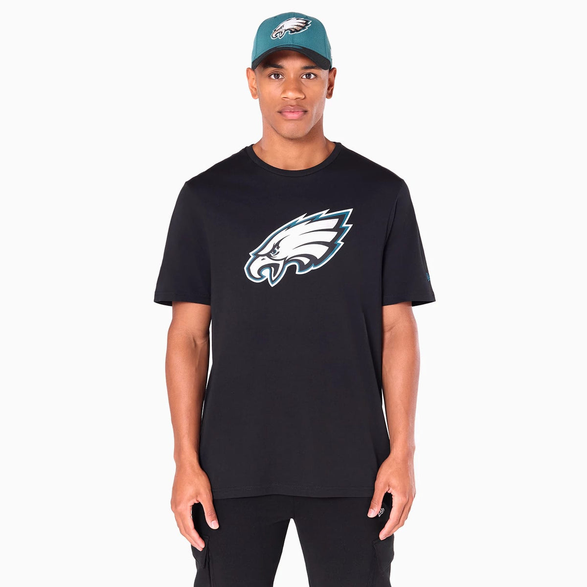 New Era Philadelphia Eagles NFL Black T-Shirt, on-model view showing the black T-shirt with a large white and teal Eagles logo centred on the chest, short sleeves, and a fitted cut, worn by a person with a teal cap featuring a raised Eagles logo.