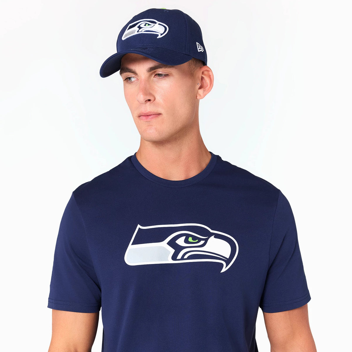 New Era Seattle Seahawks NFL Navy T-Shirt, on-model view showing a person wearing the navy T-shirt with a large white and grey Seahawks logo on the chest and a matching navy cap featuring the same logo on the front.