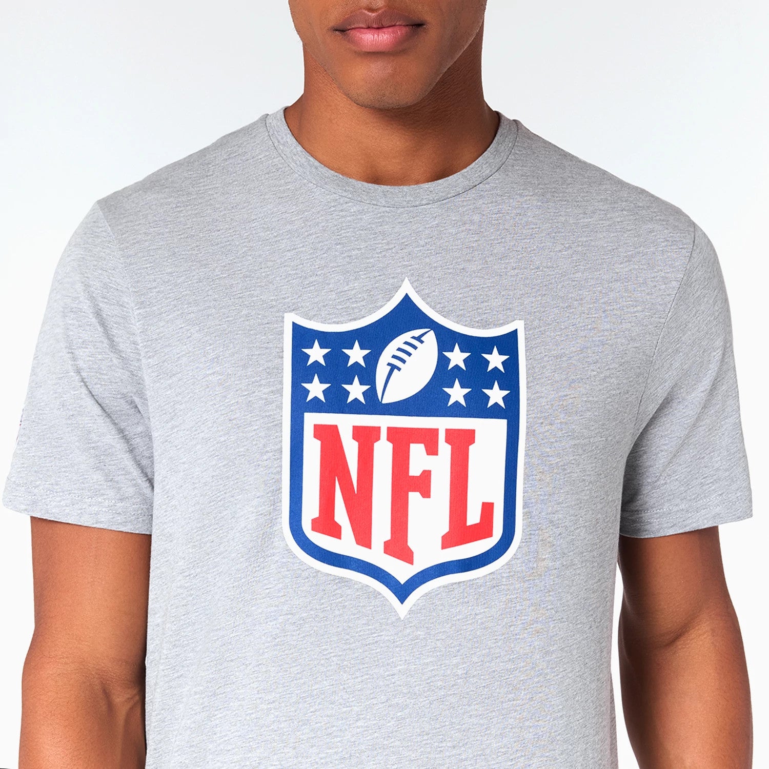 New Era NFL Shield Logo NFL Grey T-Shirt, front view featuring a large shield logo with a raised outline centred on the chest, showing a blue upper half with white stars and a football, and a red 'NFL' text on the lower half.