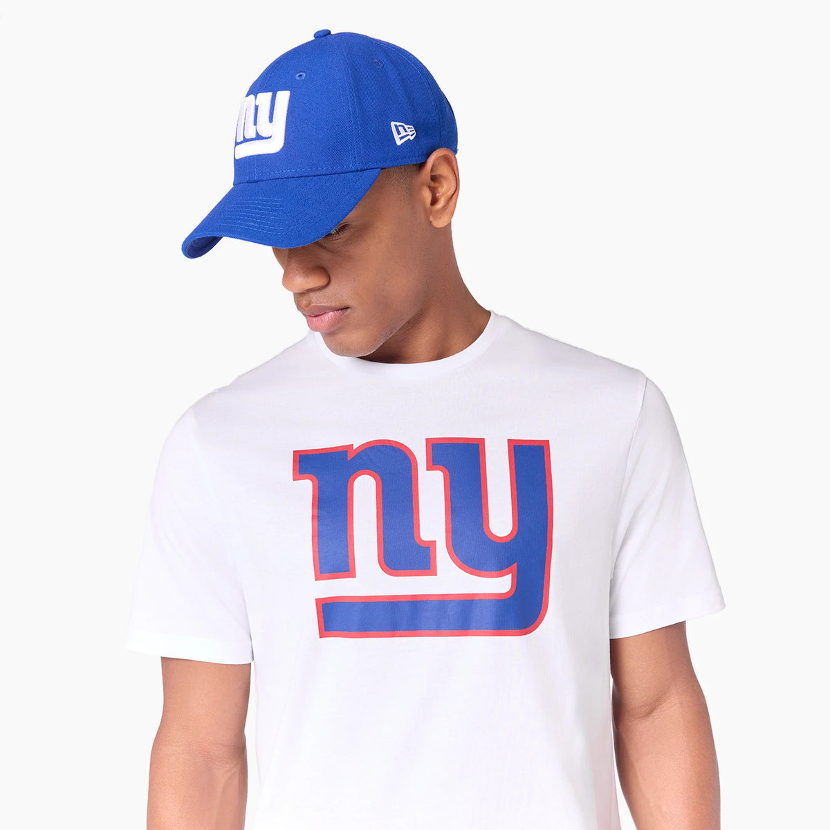 New Era New York Giants NFL White T-Shirt, on-model view showing the white shirt with a large blue and red ny logo across the chest, paired with a blue cap featuring a raised white ny logo on the front.