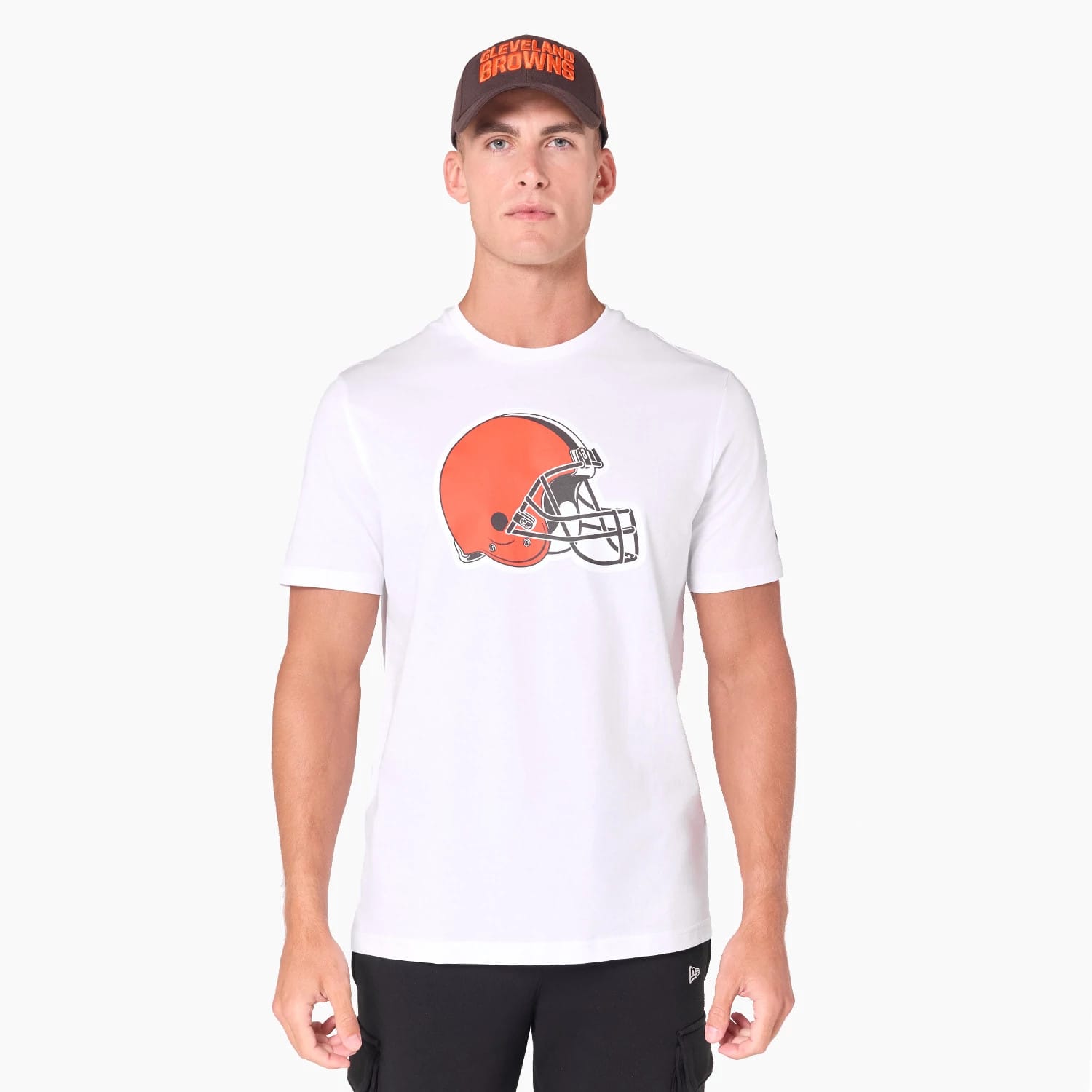 New Era Cleveland Browns NFL White T-Shirt, on-model view showing a large orange football helmet graphic centred on the chest, paired with a black cap featuring a raised Cleveland Browns logo in orange text.