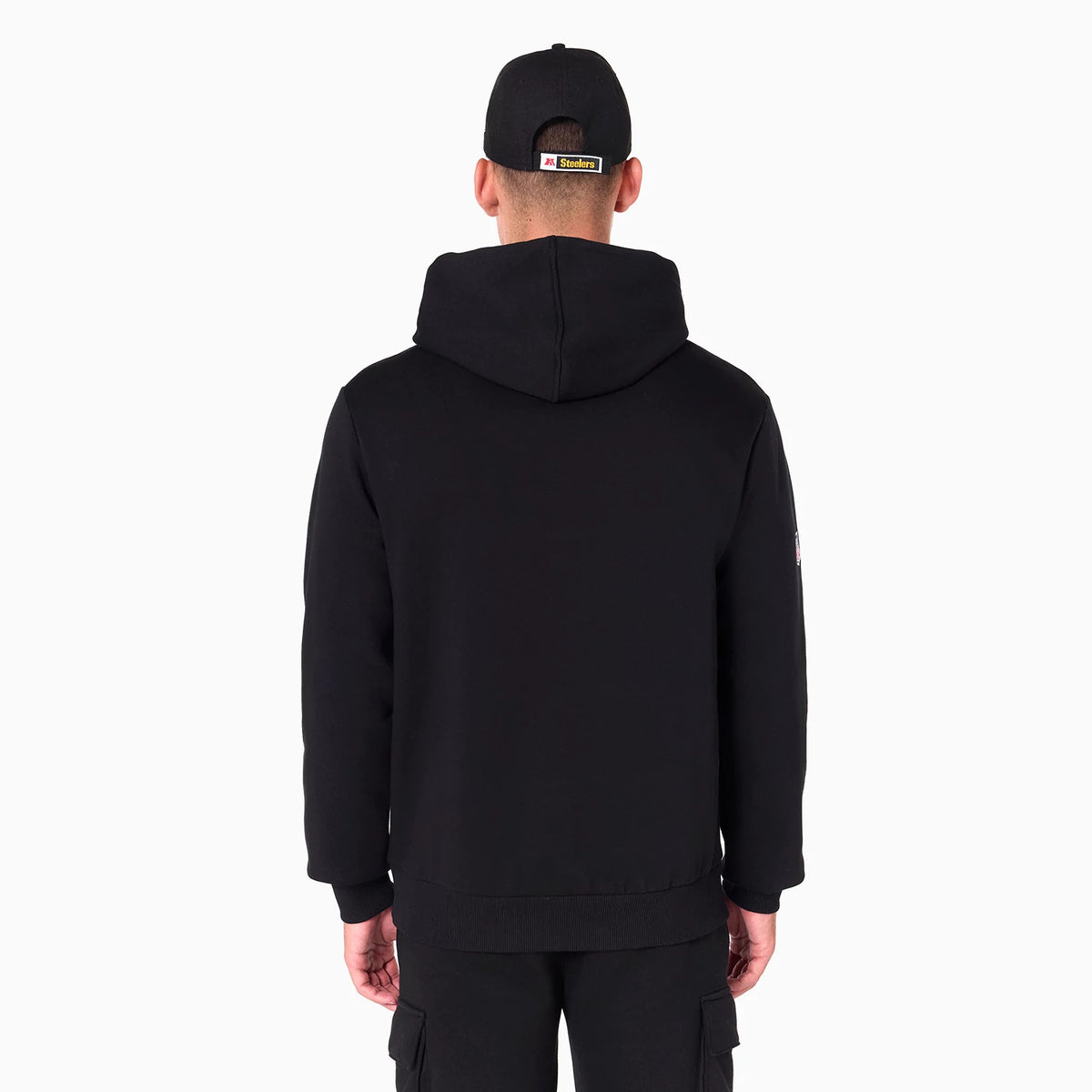 New Era Pittsburgh Steelers NFL Black Pullover Hoodie, rear view showing the black hood and simple back design, worn by a person wearing a black cap with a small embossed logo on the strap.