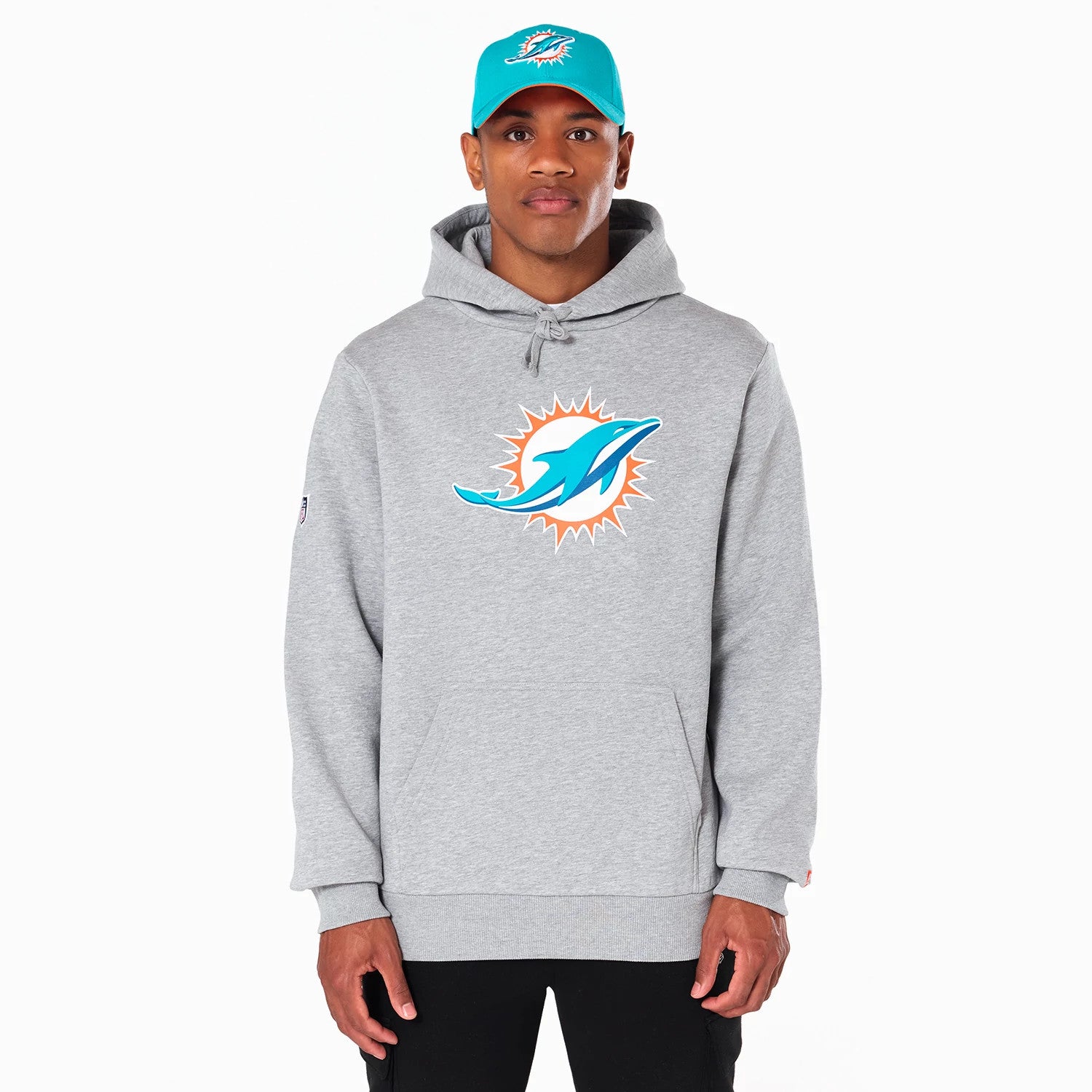 New Era Miami Dolphins NFL Grey Pullover Hoodie, on-model view featuring a large team logo in teal and orange centred on the chest, worn with a teal cap displaying the same logo, showing the hood and front pocket details.