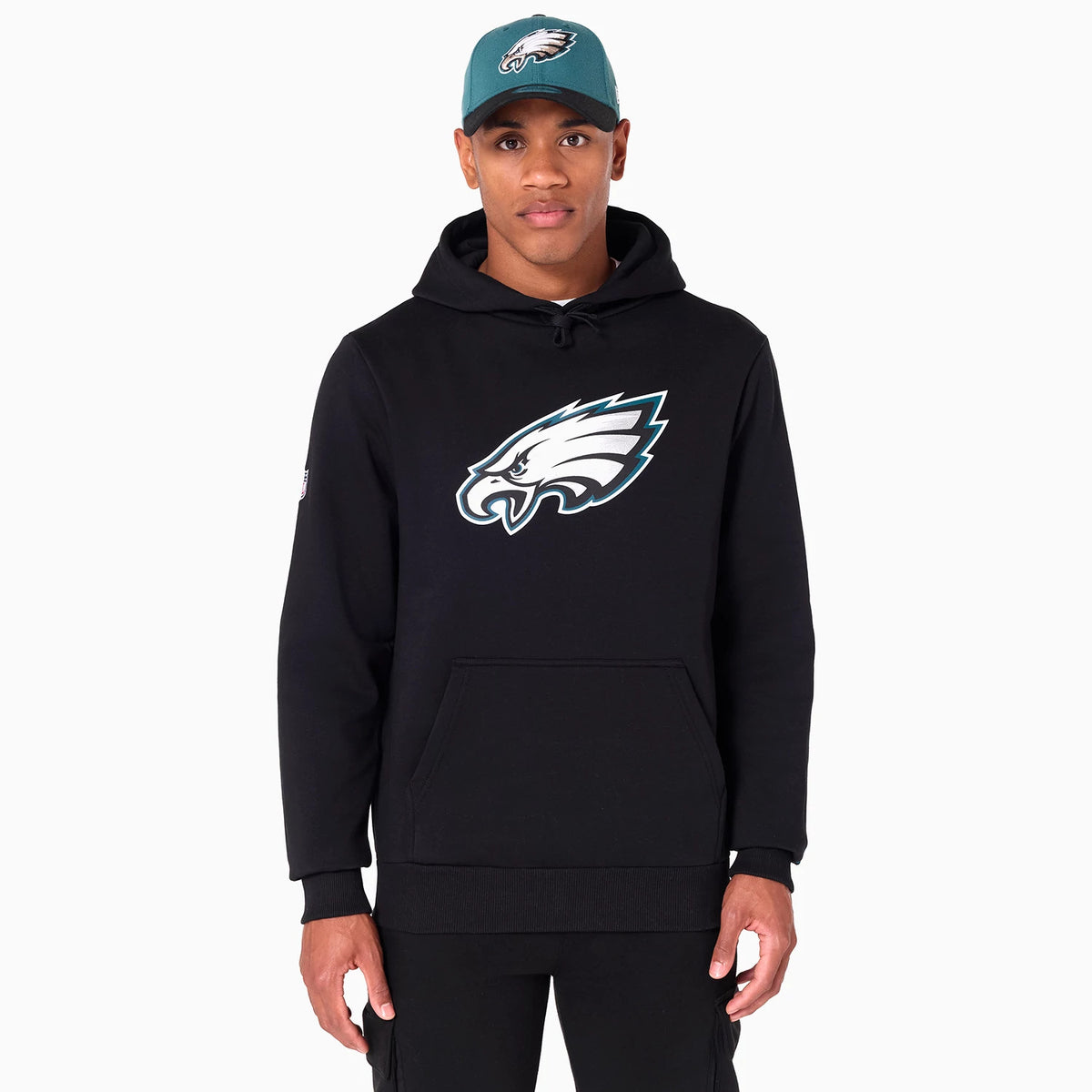 New Era Philadelphia Eagles NFL Black Pullover Hoodie, front view showing a black hoodie worn with a large white eagle logo on the chest and a teal cap on the model featuring the same logo on the front.