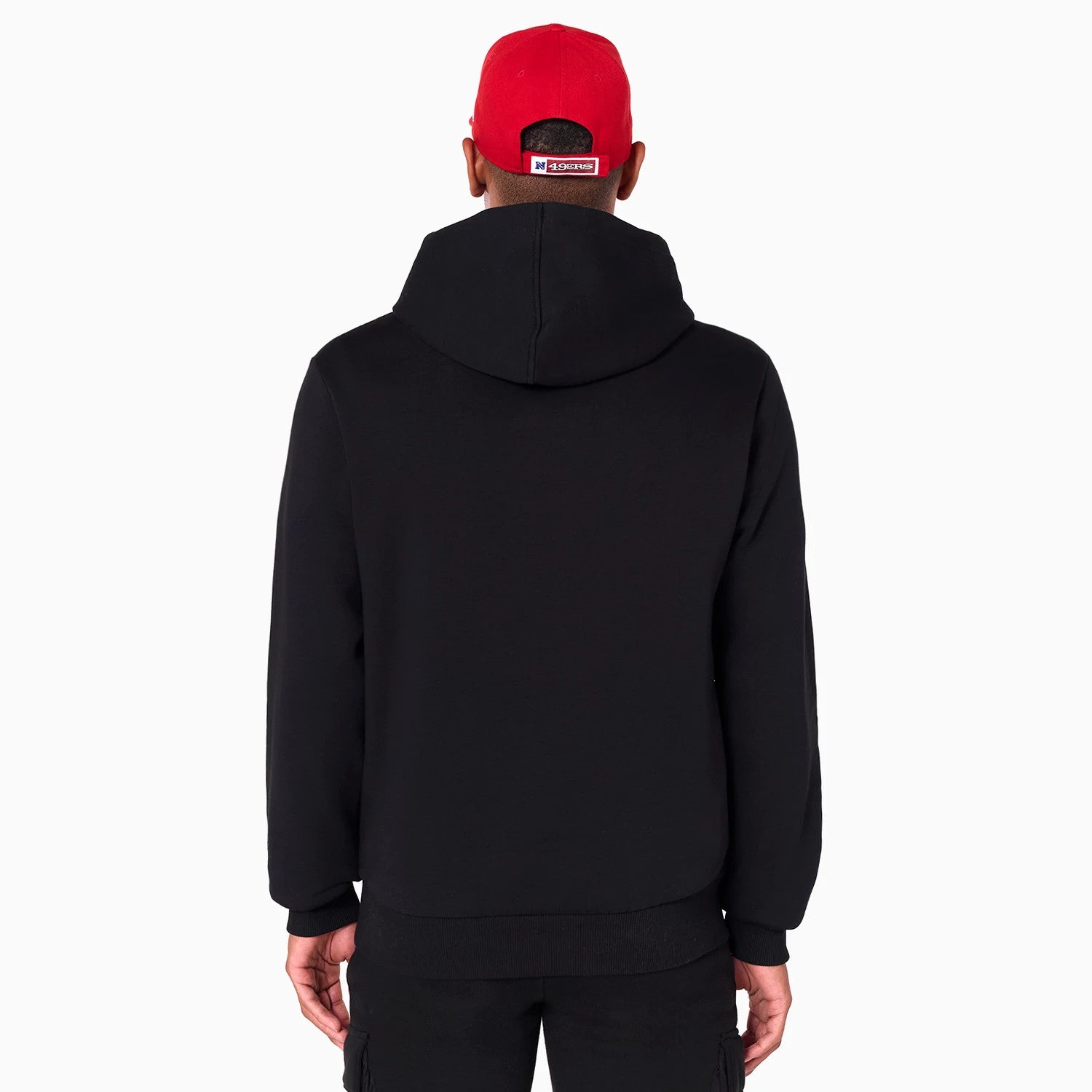 New Era San Francisco 49ers NFL Black Pullover Hoodie, rear view showing the plain black back with a large hood, worn by a model in black trousers and a red cap with a debossed logo.