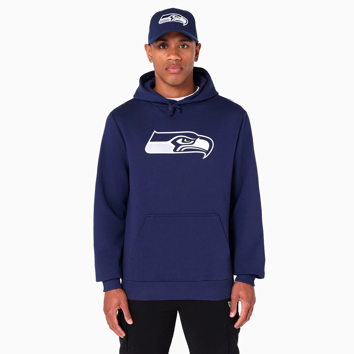 New Era Seattle Seahawks NFL Navy Pullover Hoodie, front view showing the large team logo printed in white and blue across the chest, with a kangaroo pocket below and a matching navy cap featuring an embroidered logo on a model.