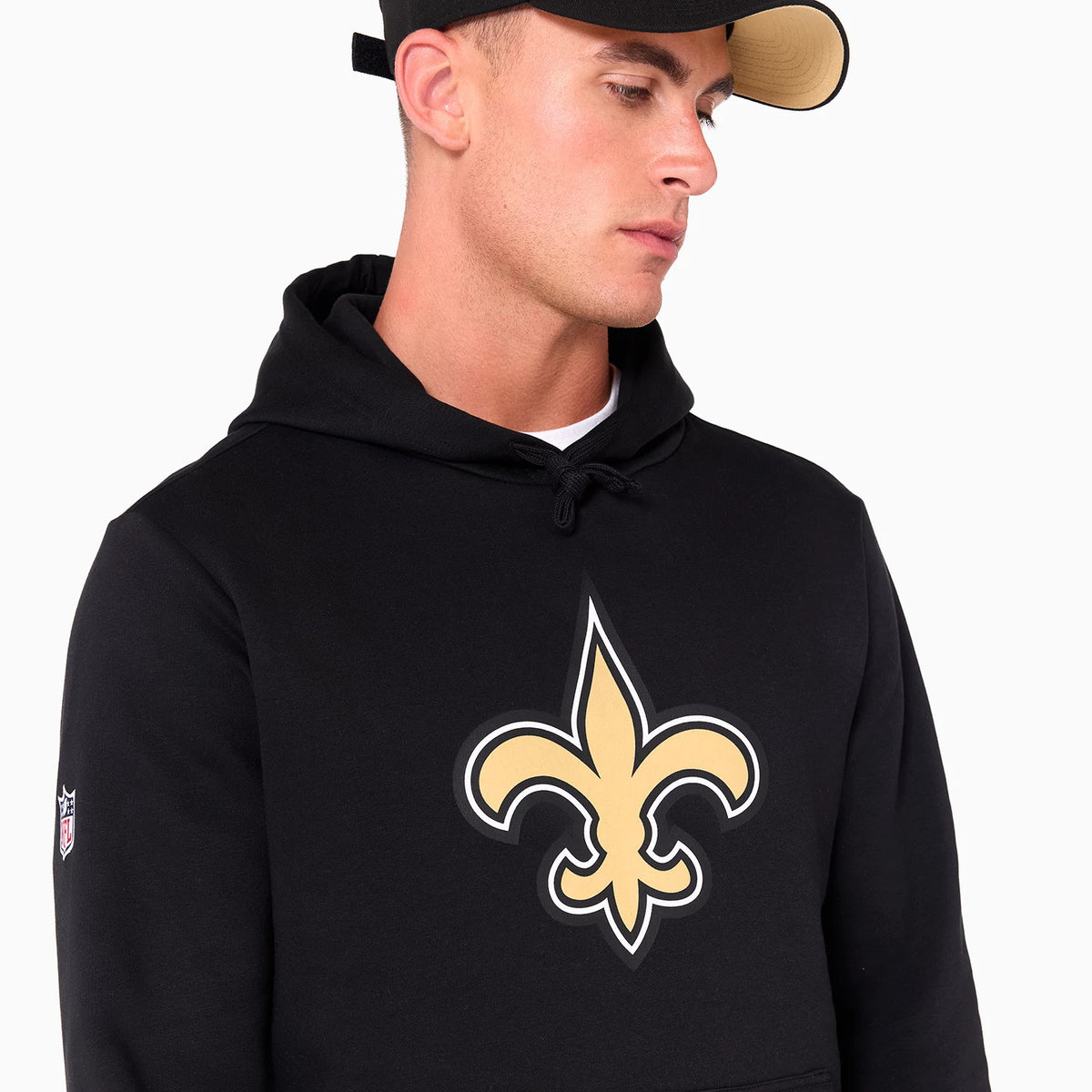 New Era New Orleans Saints NFL Black Pullover Hoodie, front view showing a large central fleur-de-lis symbol in gold and white on the chest, with the NFL logo patch on the sleeve and a black drawstring on the hood.