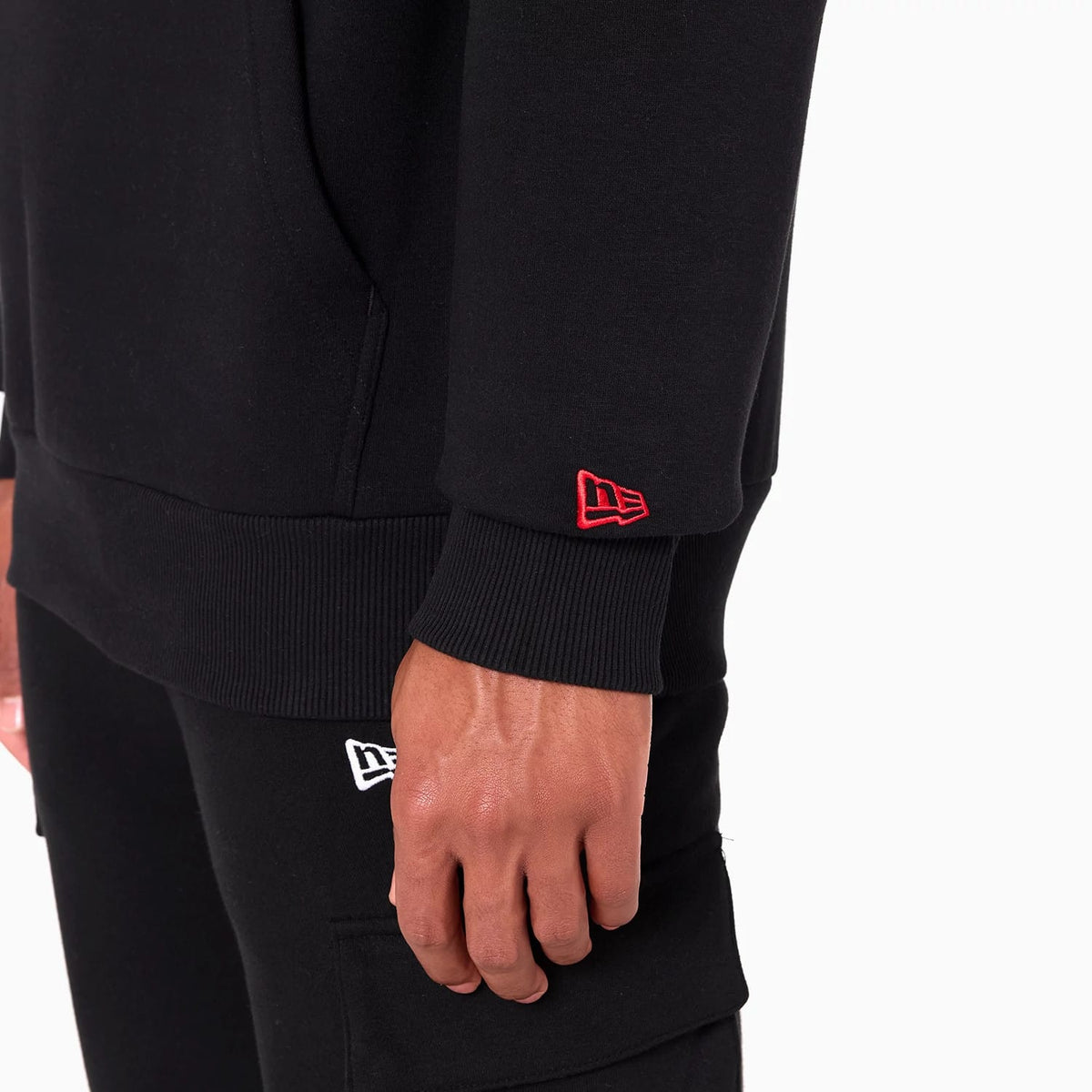 New Era Kansas City Chiefs NFL Black Pullover Hoodie, side view showing the black sleeve with a ribbed cuff and a red embroidered New Era logo near the wrist, worn by a model with matching black trousers.