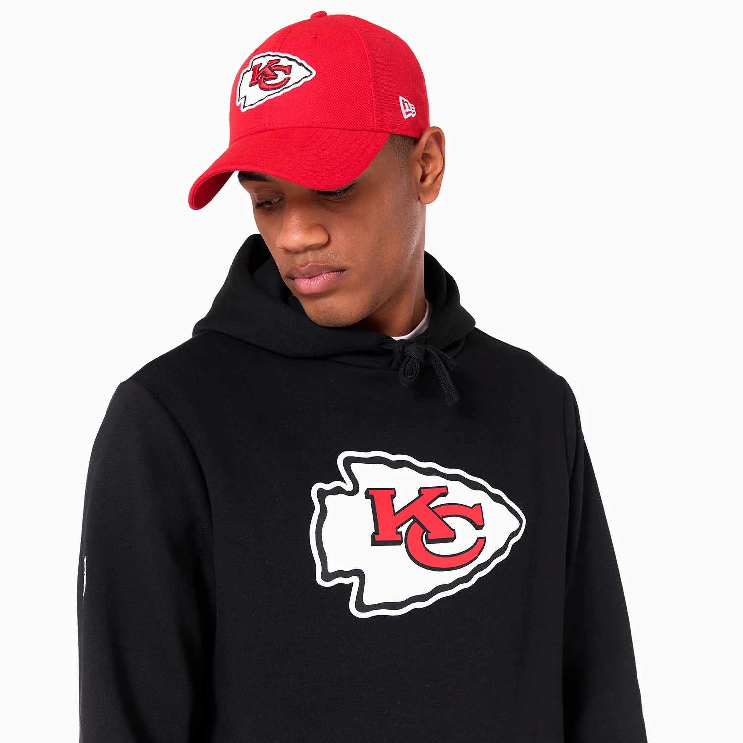 New Era Kansas City Chiefs NFL Black Pullover Hoodie, on-model view showing a large red and white team logo printed on the chest, paired with a red cap featuring a raised New Era logo on the side.