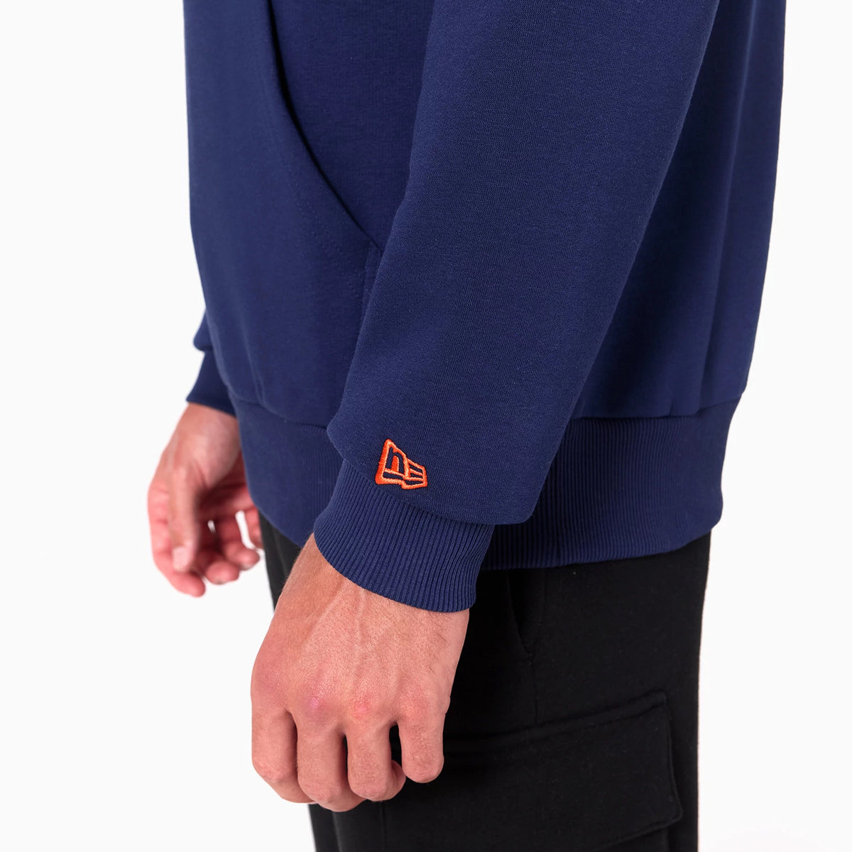 New Era Denver Broncos NFL Navy Pullover Hoodie, side view showing a blue sleeve with a ribbed cuff and an orange embroidered New Era logo near the wrist, part of the body and pocket visible above the hem.