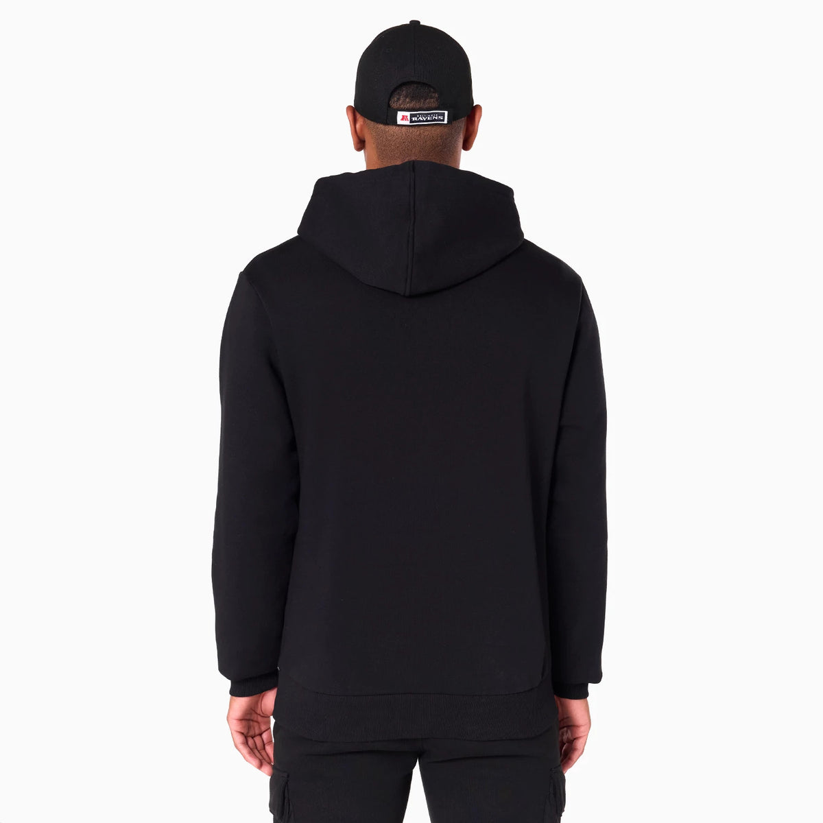 New Era Baltimore Ravens NFL Black Pullover Hoodie, rear view showing the plain black back with a hood lying flat, worn by a model also wearing a black cap with an embroidered logo centred on the back above the adjustable strap.