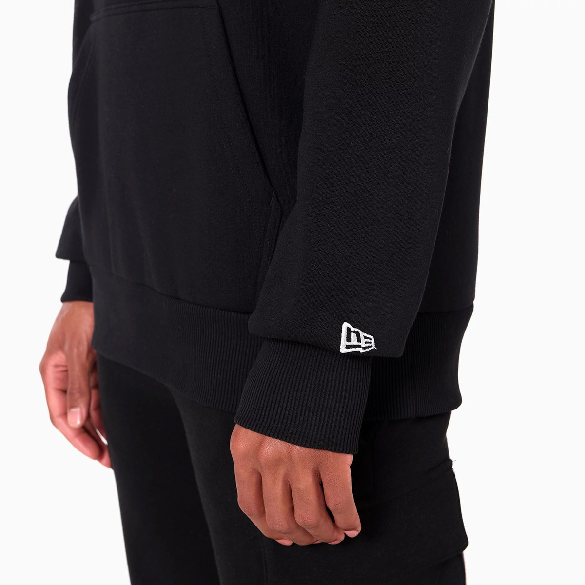 New Era Atlanta Falcons NFL Black Pullover Hoodie, side view showing the ribbed cuff on the sleeve, a raised New Era logo embroidered near the wrist, and the edge of the kangaroo pocket on the black fabric.