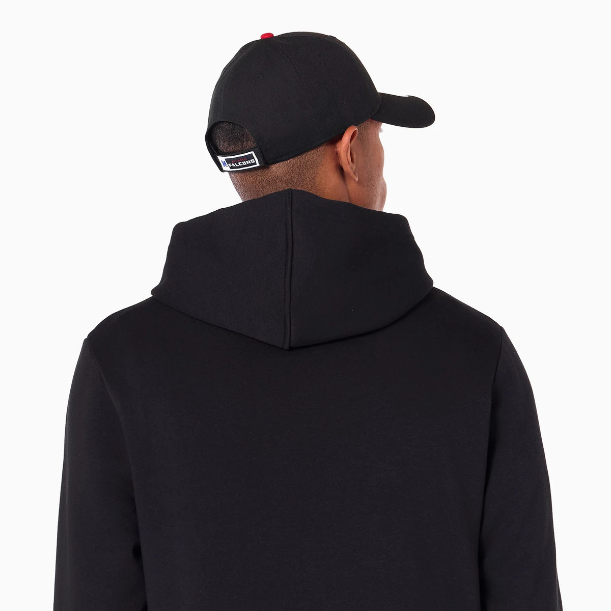 New Era Atlanta Falcons NFL Black Pullover Hoodie, rear view showing the plain black hood resting on the back, worn by a person with a black cap featuring a raised logo above the opening.