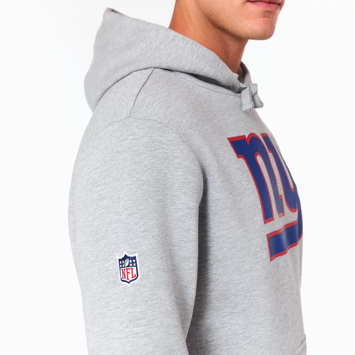New Era New York Giants NFL Grey Pullover Hoodie, side view showing a grey hoodie with a blue and red embroidered ny logo across the chest and an NFL shield logo on the upper left sleeve.