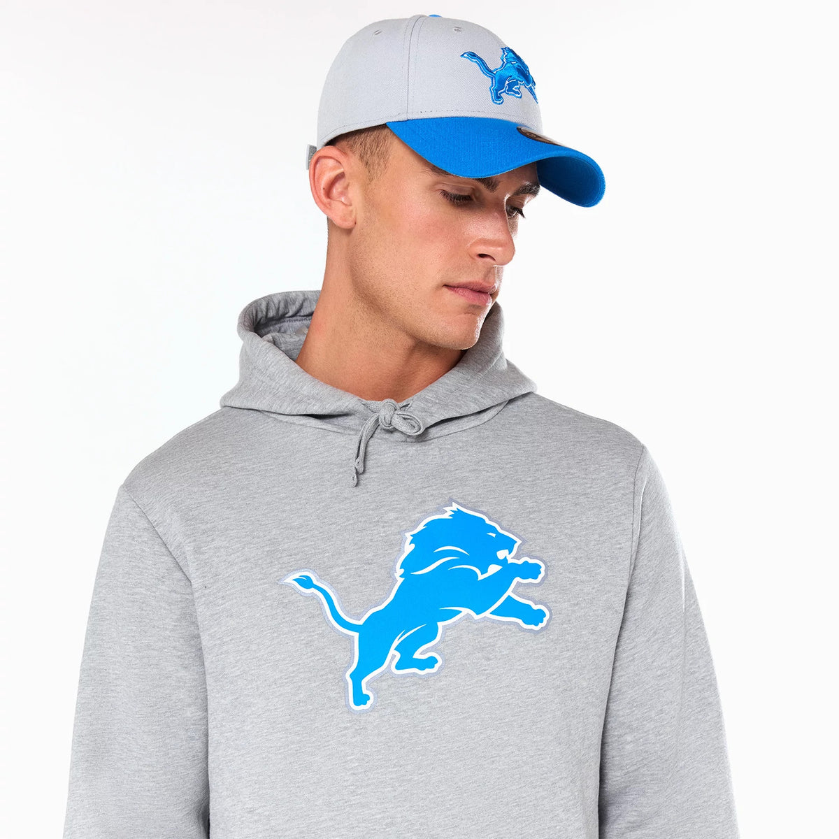 New Era Detroit Lions NFL Grey Pullover Hoodie, on-model view showing a large blue lion logo embossed on the chest, matched with a grey and blue cap featuring an embossed lion logo on the front.