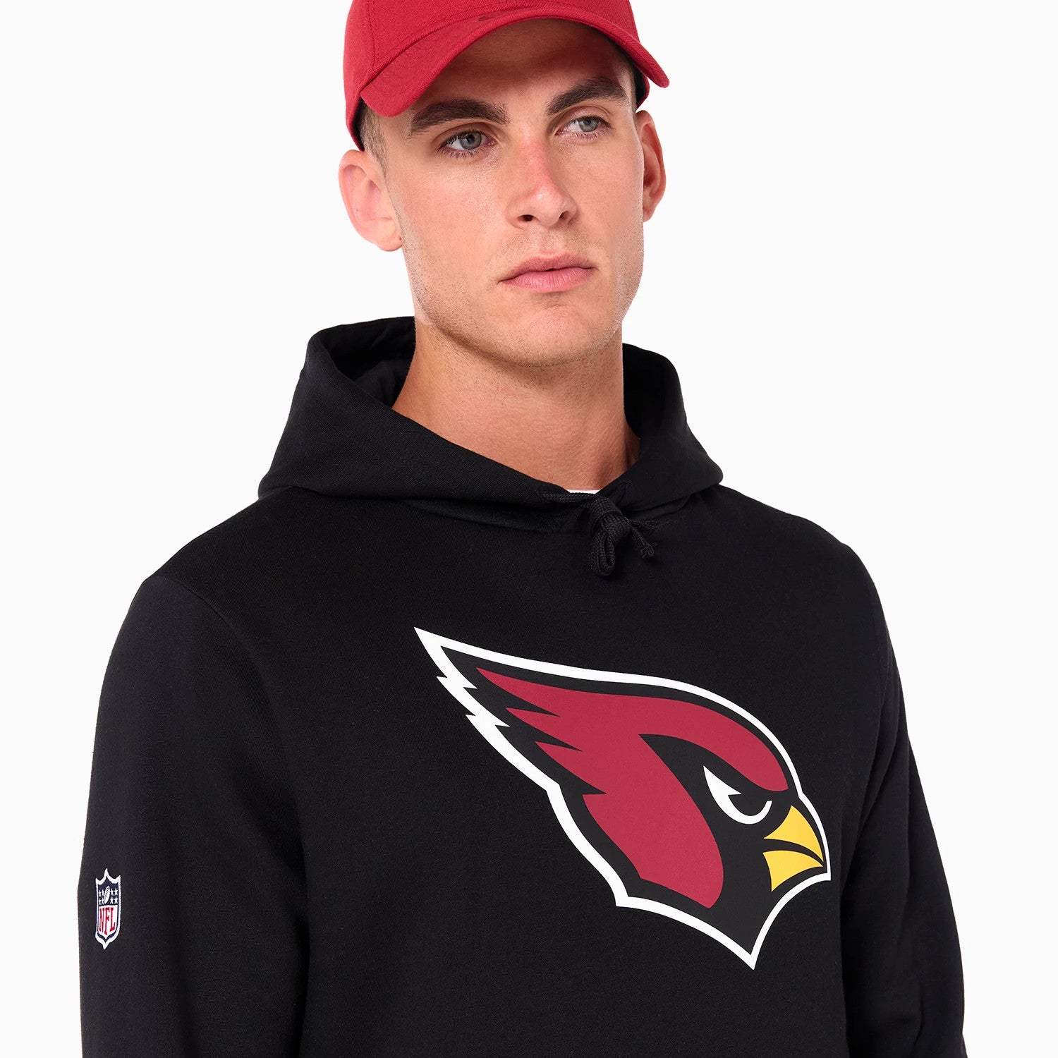 New Era Arizona Cardinals NFL Black Pullover Hoodie, on-model view showing the large Cardinals logo in red and white across the chest, a drawstring hood, and a raised NFL logo on the left sleeve worn by a person in a red cap.