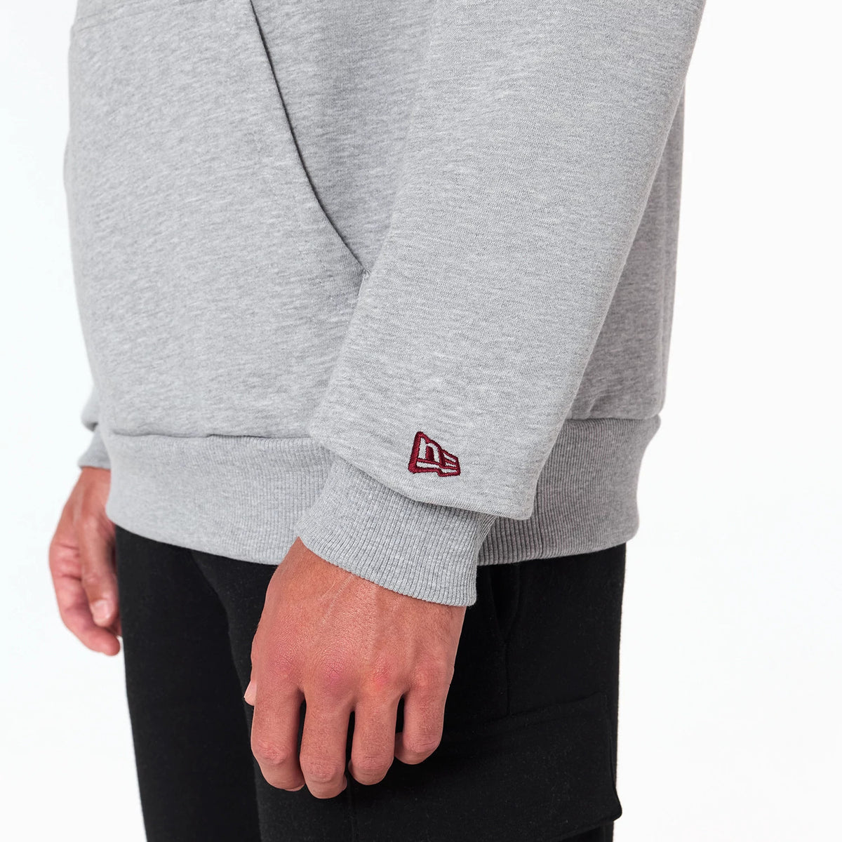 New Era Washington Commanders NFL Grey Pullover Hoodie, side view showing the lower sleeve featuring a small raised burgundy New Era logo near the cuff and the soft grey fabric extending over the wrist.