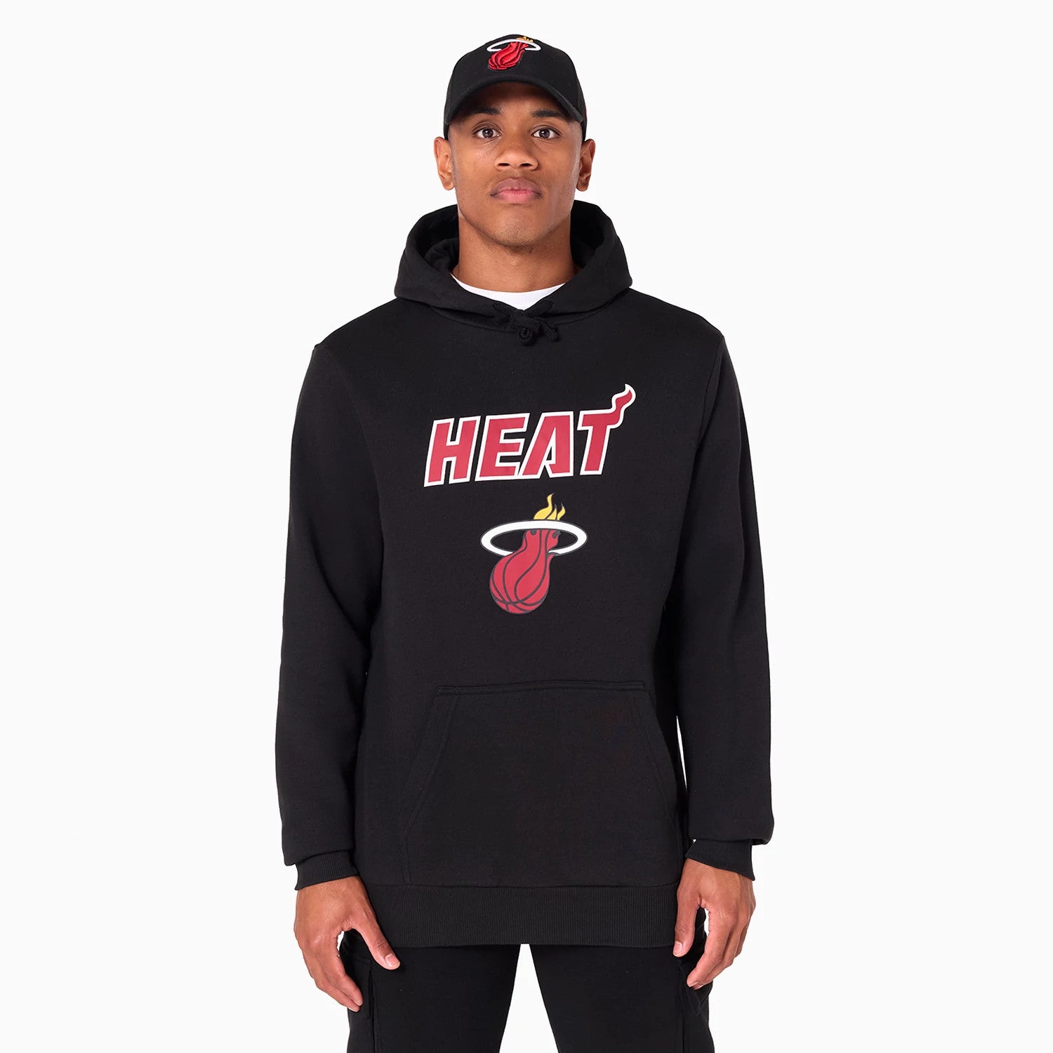 New Era Miami Heat NBA Black Pullover Hoodie, front view showing a large heat logo emblazoned in white, red, and yellow on the chest with a drawstring hood, paired with a black cap featuring an embroidered Miami Heat logo.