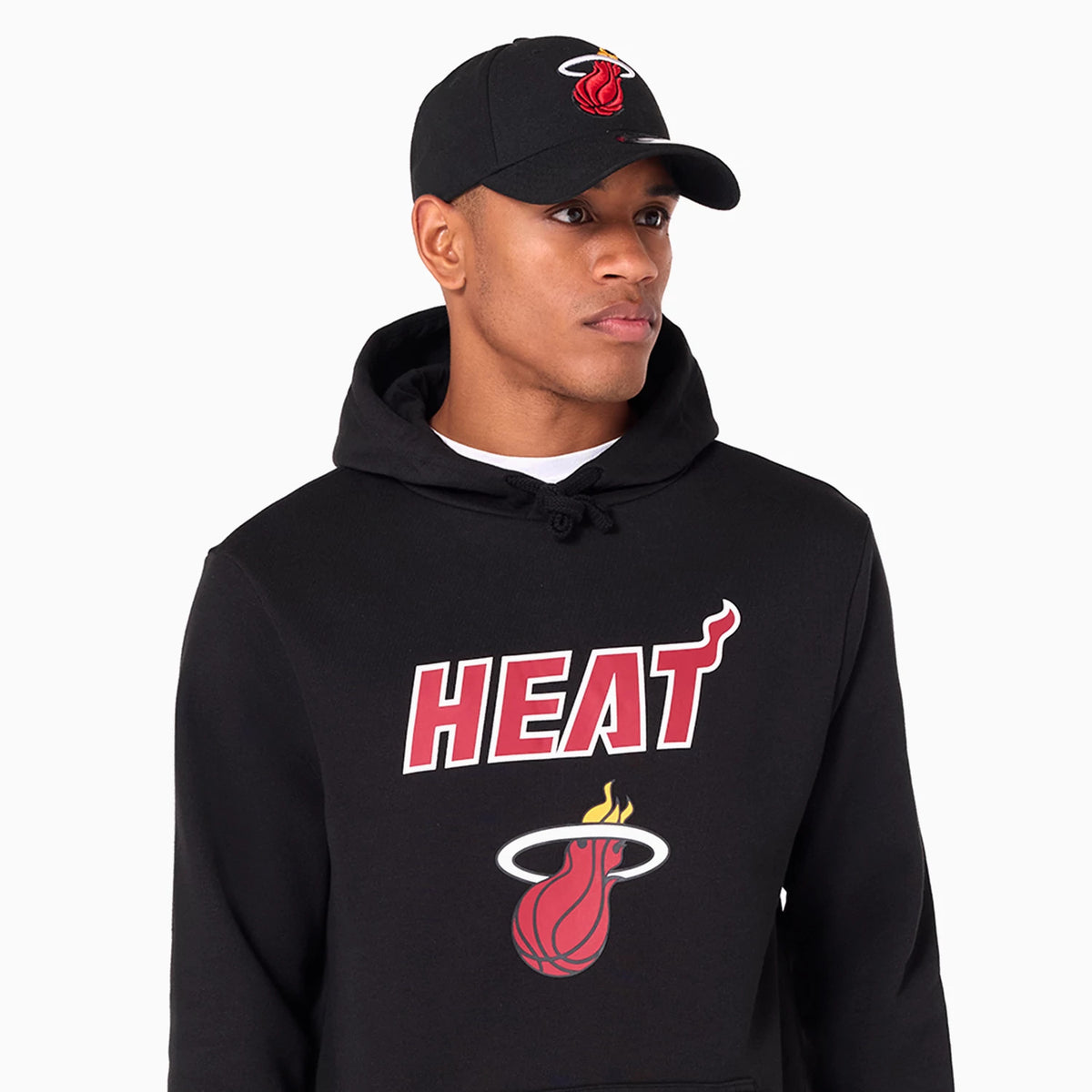 New Era Miami Heat NBA Black Pullover Hoodie, on-model view showing the large Heat logo printed across the front chest, with a black drawstring hood and a model wearing a black cap featuring a raised Heat logo on the front.