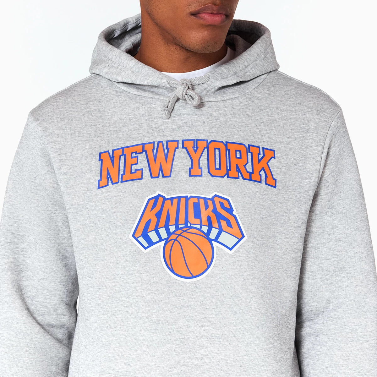 New Era New York Knicks NBA Grey Pullover Hoodie, front view showing the grey fabric with a large orange and blue Knicks logo across the chest, drawstrings at the hood, and a relaxed fit on the model.