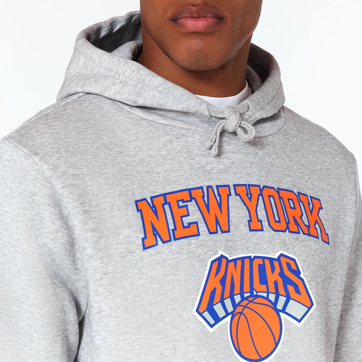 New Era New York Knicks NBA Grey Pullover Hoodie, front view showing a grey hoodie with NEW YORK KNICKS printed in orange and blue on the chest, featuring a basketball graphic below the text, with a drawstring hood.