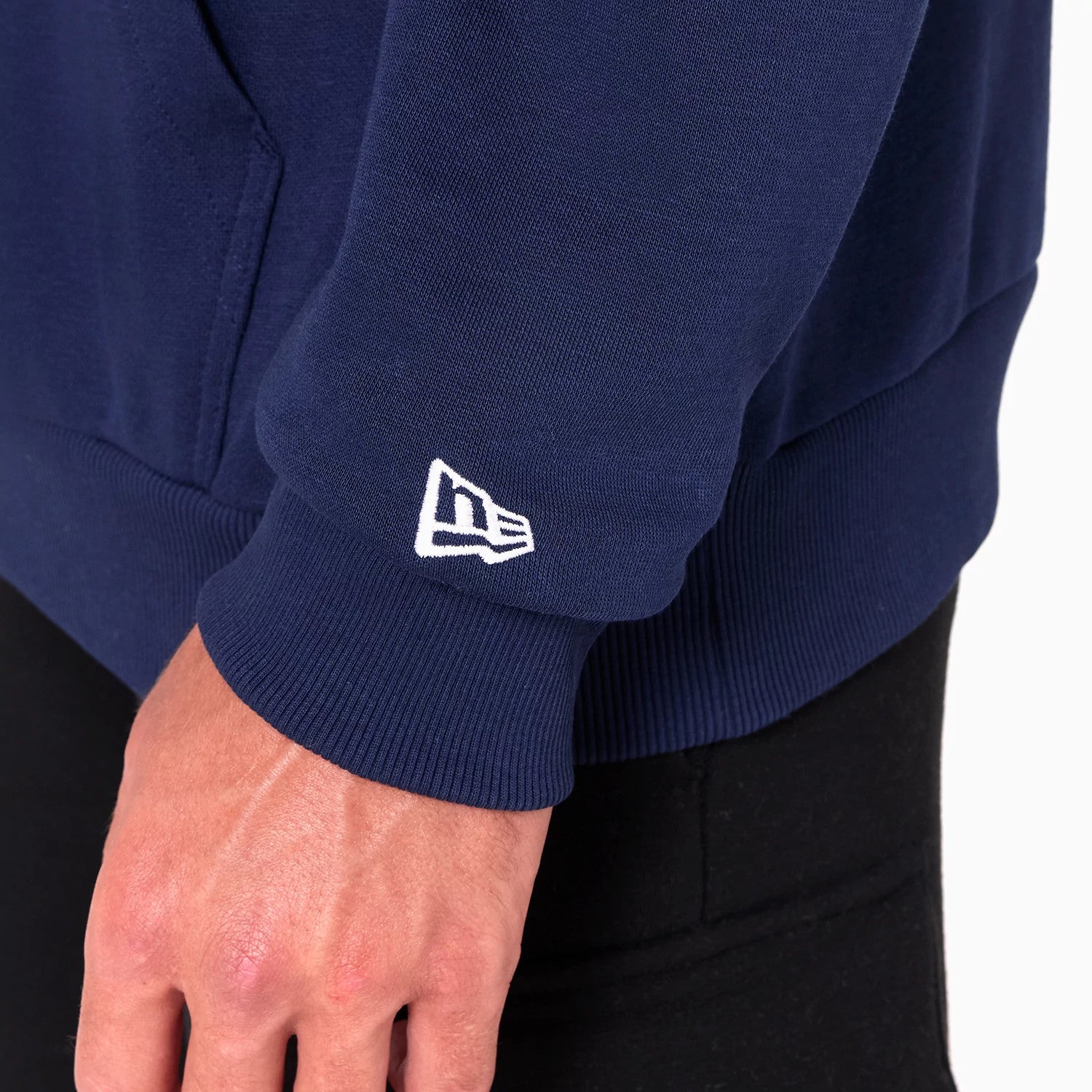 New Era Detroit Pistons NBA Navy Pullover Hoodie, on-model view showing a ribbed cuff sleeve with a white embroidered New Era logo near the wrist on the navy fabric, highlighting the casual design above black trousers.