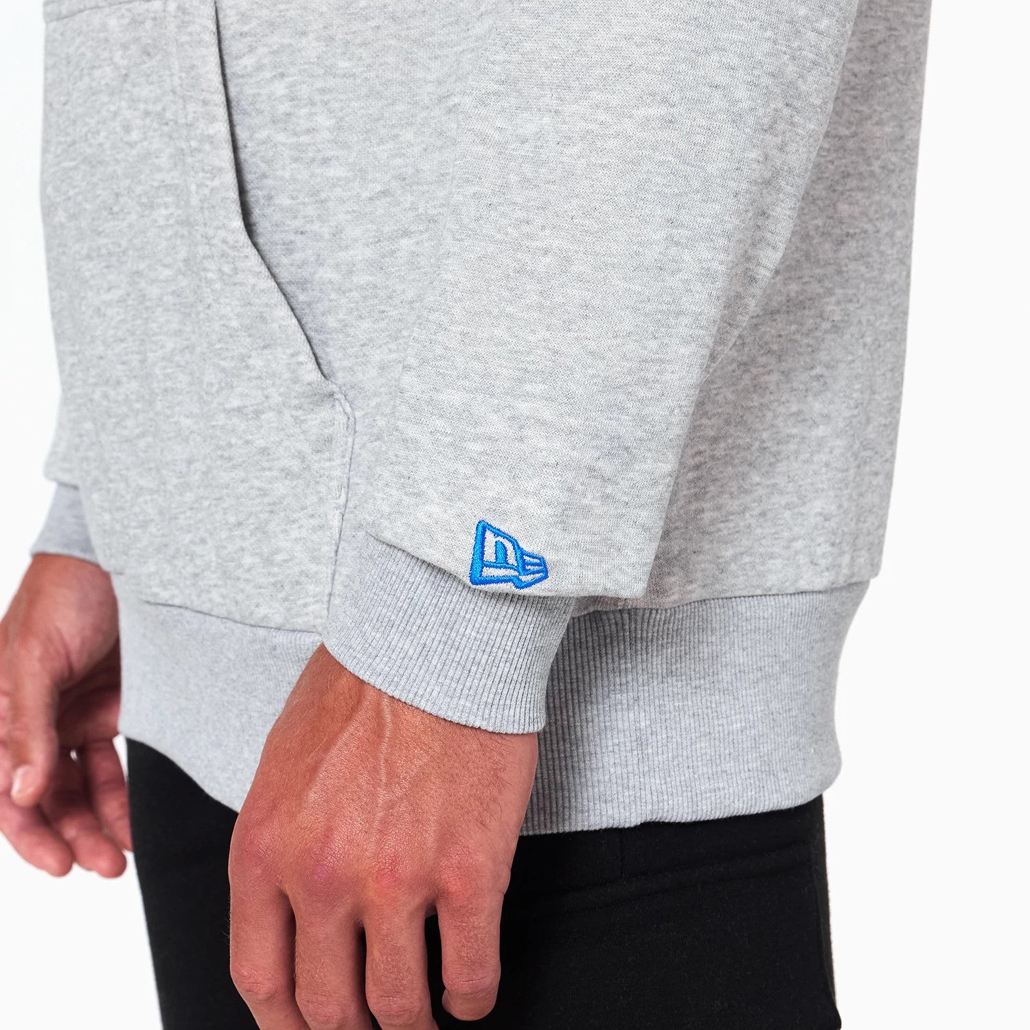 New Era Dallas Mavericks NBA Grey Pullover Hoodie, side view showing a light grey ribbed cuff on the sleeve with a blue embroidered New Era logo near the wrist and part of a front kangaroo pocket.