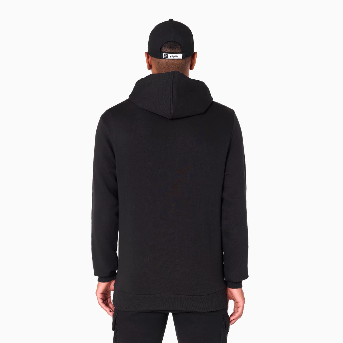 New Era San Antonio Spurs NBA Black Pullover Hoodie, rear view showing the plain black back with the hood resting on the shoulders, worn by a person also wearing a black cap with a label above the adjustable strap.