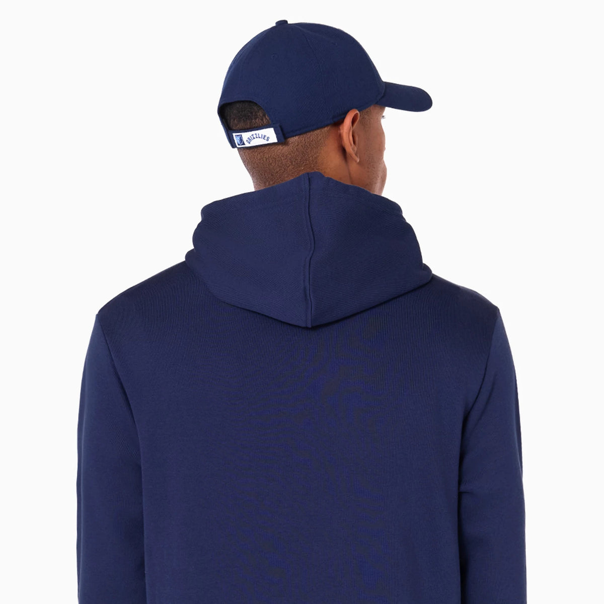New Era Memphis Grizzlies NBA Navy Pullover Hoodie, on-model rear view showing the solid navy colour with a raised hood, paired with a matching navy cap featuring a debossed logo on the back strap.