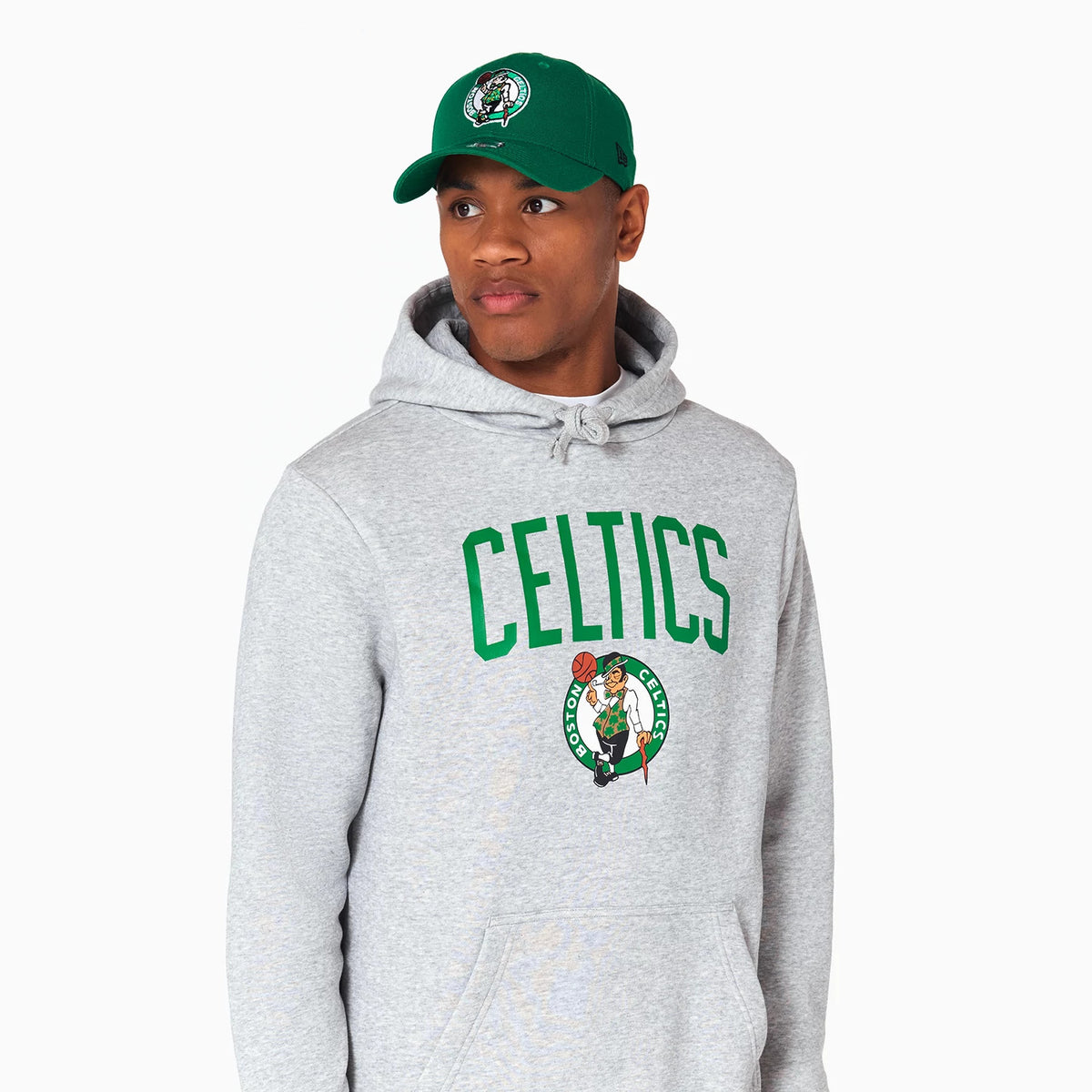 New Era Boston Celtics NBA Grey Pullover Hoodie, on-model view showing the grey fabric with a green CELTICS text across the chest and a large Boston Celtics logo below, paired with a green cap featuring a raised Celtics logo.