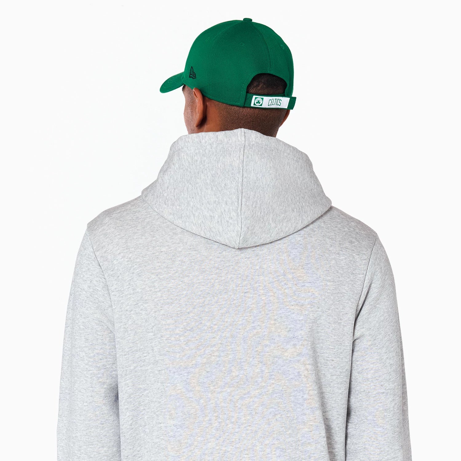 New Era Boston Celtics NBA Grey Pullover Hoodie, rear view showing the grey fabric and hood from behind, paired with a green cap featuring a debossed New Era logo on the side and an embroidered Celtics logo on the back strap.
