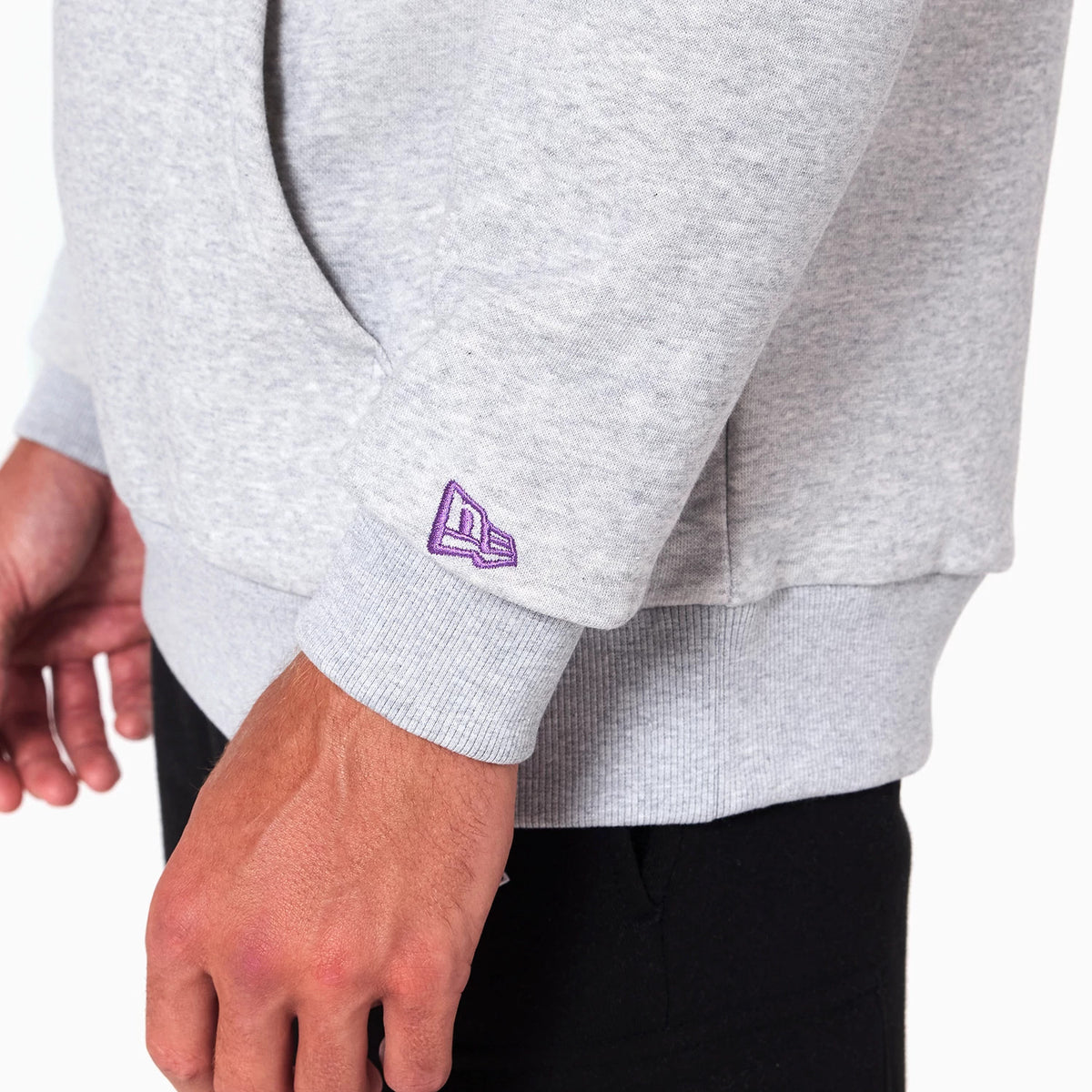 New Era Sacramento Kings NBA Grey Pullover Hoodie, side view showing a ribbed cuff on the long sleeve with a purple embroidered New Era logo near the wrist, and the light grey fabric worn with black trousers.