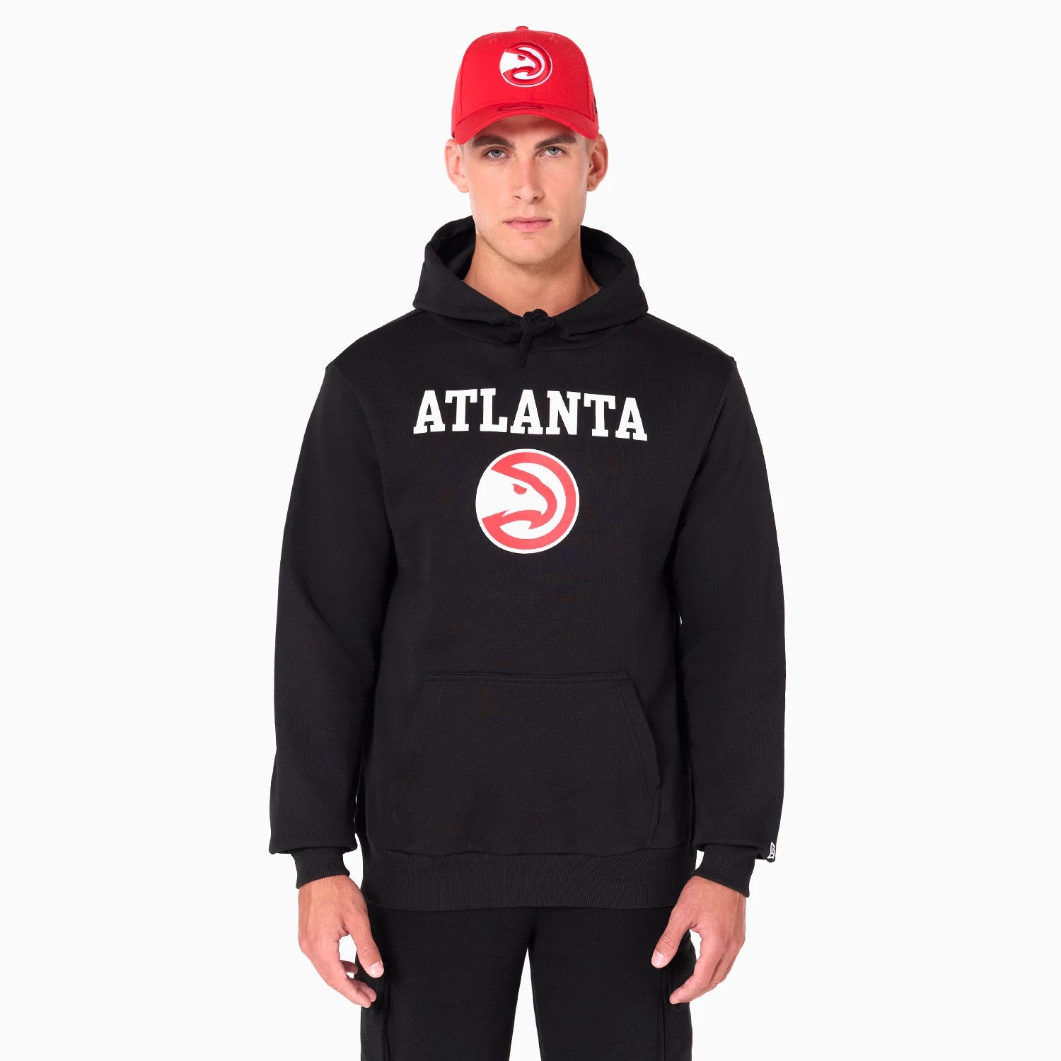 New Era Atlanta Hawks NBA Black Pullover Hoodie, on-model view showing the black hoodie with 'ATLANTA' text and Hawks logo on the chest, featuring a drawstring hood, and the model wearing a red cap with debossed logo.