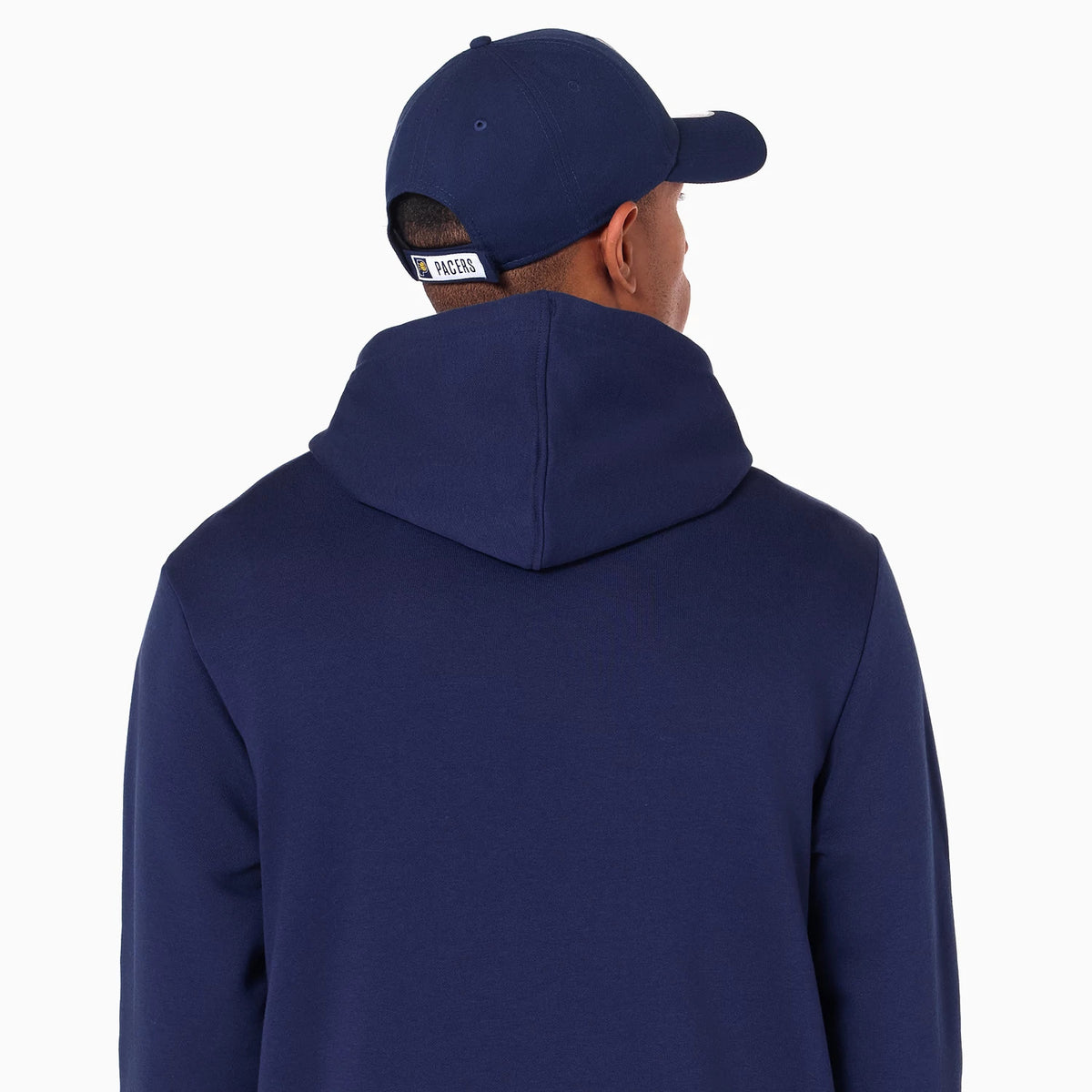 New Era Indiana Pacers NBA Navy Pullover Hoodie, on-model rear view showing the plain navy hood in a raised position and a navy cap with a debossed Indiana Pacers logo on the back strap.