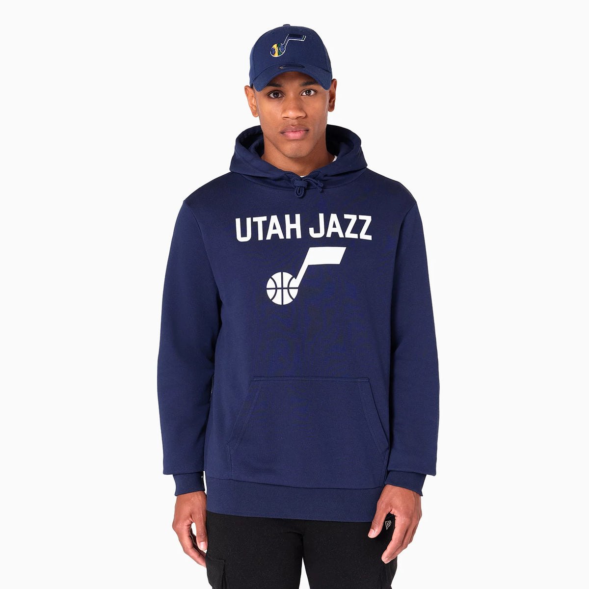 New Era Utah Jazz NBA Navy Pullover Hoodie, on-model view showing the navy hoodie with a large white Utah Jazz logo on the chest, drawstring hood, front pocket and a raised embroidered New Era logo on a blue cap worn by the model.