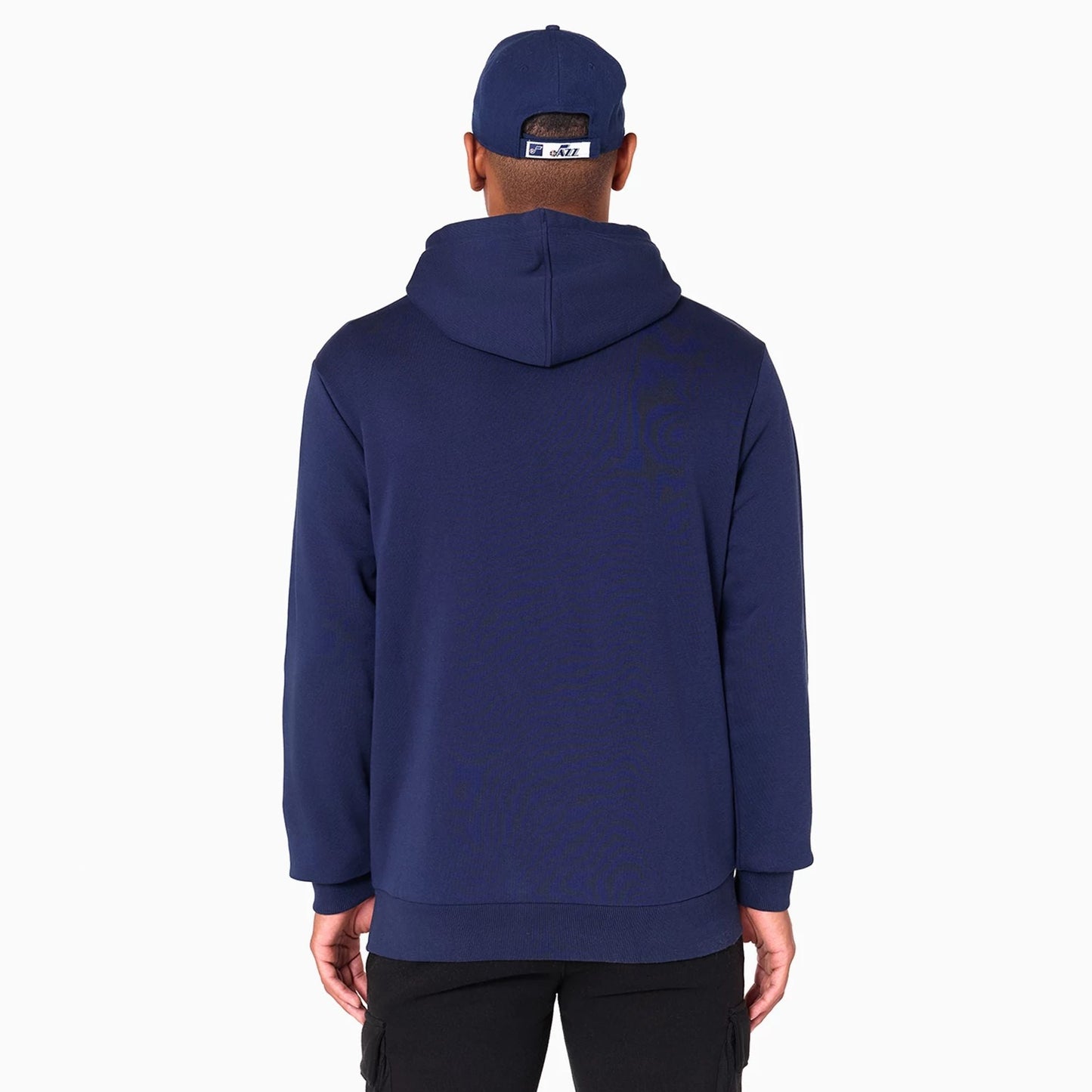 New Era Utah Jazz NBA Navy Pullover Hoodie, rear view showing the back of the navy hoodie with a relaxed fit, attached hood, and a person wearing a matching navy cap with a raised logo on the back above the adjustable strap.