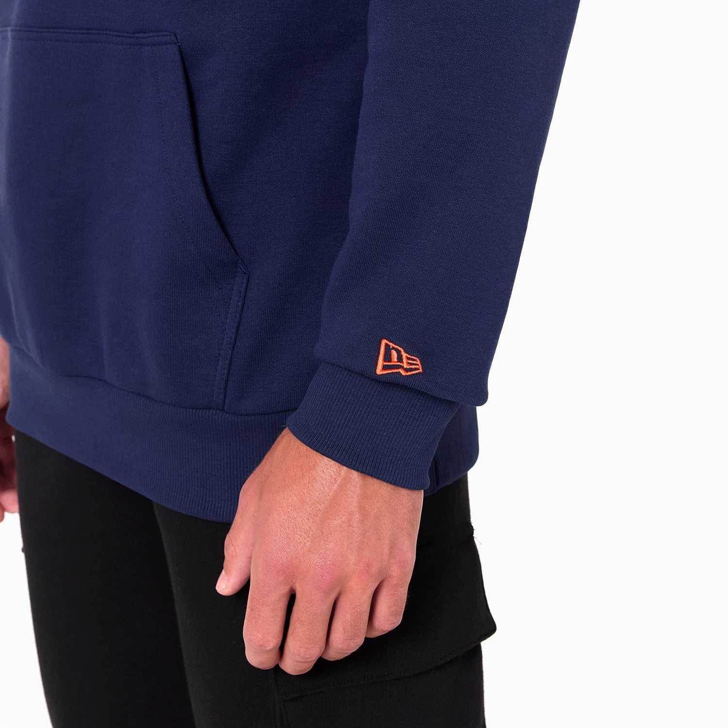 New Era Oklahoma City Thunder NBA Navy Pullover Hoodie, side view showing the ribbed cuff with an orange raised New Era logo on the sleeve, a large front pouch pocket on the navy fabric and part of the hem at the bottom.