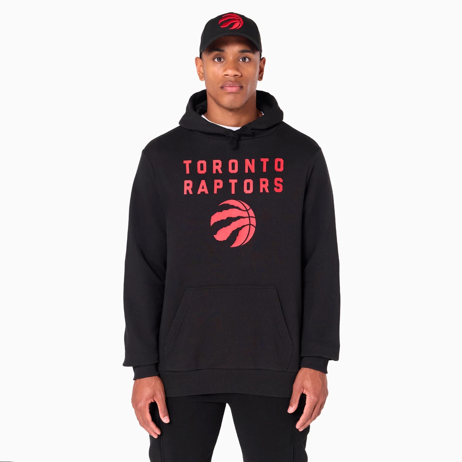New Era Toronto Raptors NBA Black Pullover Hoodie, front view showing large red Toronto Raptors text and logo centred on the chest, with a black cap featuring a raised red Raptors logo worn by the model.