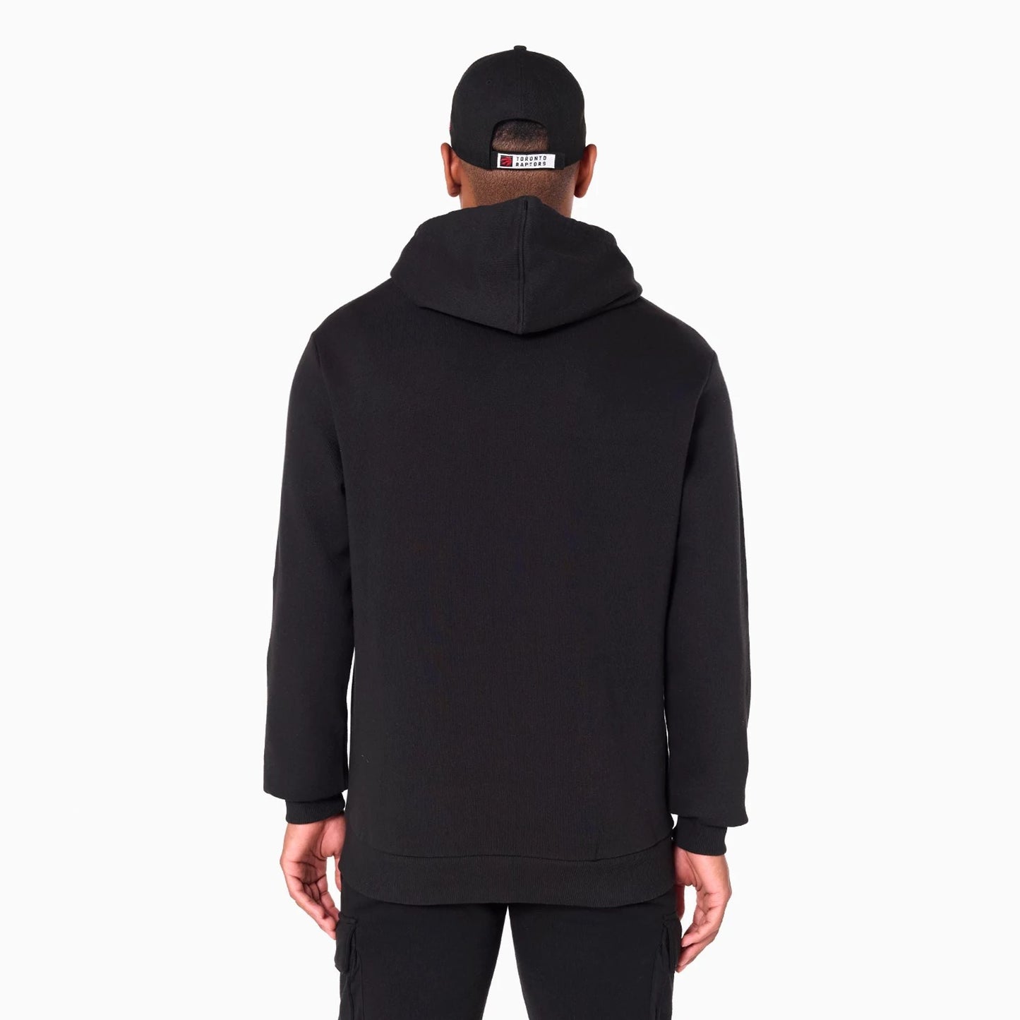 New Era Toronto Raptors NBA Black Pullover Hoodie, rear view showing the relaxed fit black hoodie with a spacious hood, worn by a model along with a black cap featuring an embroidered patch on the back.